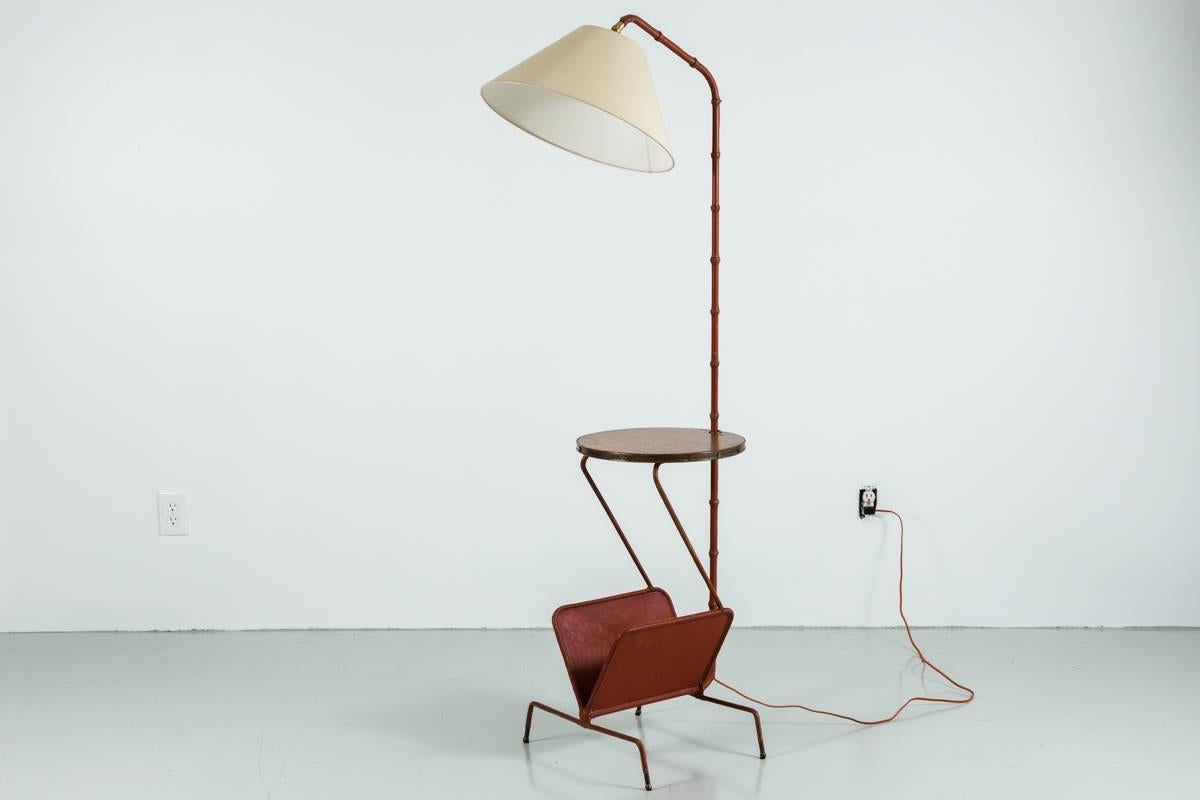 Rare Jacques Adnet floor lamp in cognac colored leather. The entire lamp is wrapped in leather with signature contrast stitching. Original wood table with brass hardware. Leather magazine holder at the bottom. Lamp sits on brass feet. Entire piece