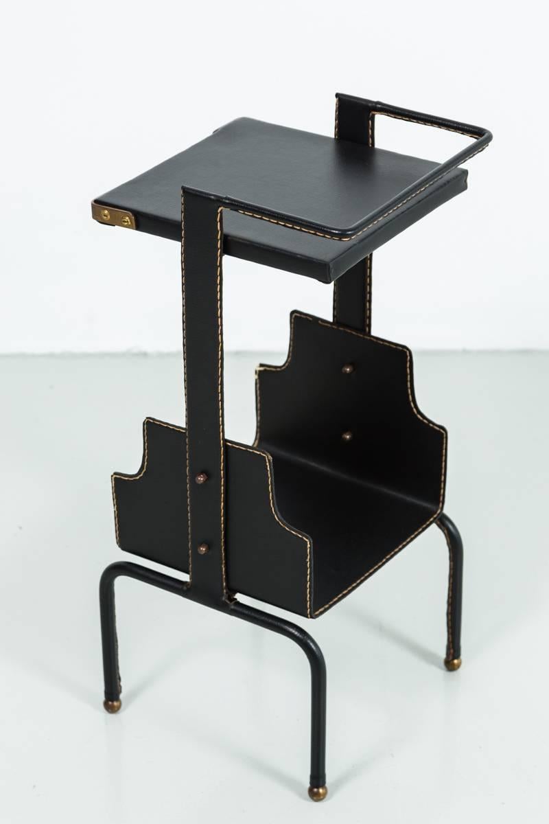 Handsome black leather side table attributed to Jacques Adnet. Signature contrast stitching with brass hardware. Excellent dark patina to brass. Excellent vintage condition. Very unique piece.