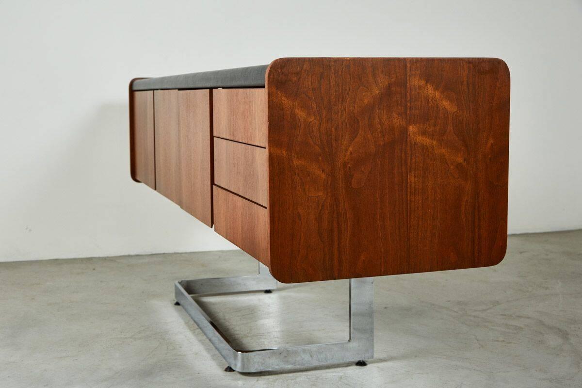 Ste-Marie and Laurent credenza with black inset leather top, one deep file drawer on one side, three pencil drawers on the right side, flanking two center doors opening into a cabinet for storage.
Cantilevered onto a polished chrome
