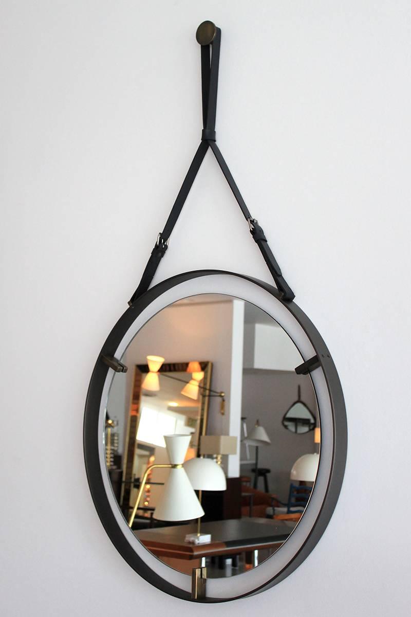 Large-scale and expertly crafted design of a floating mirror with iron frame and thick brass detail.
Leather strap and brass buckle.
Brass square hanging puck.

Overall drop with Adjustable Strap: 56