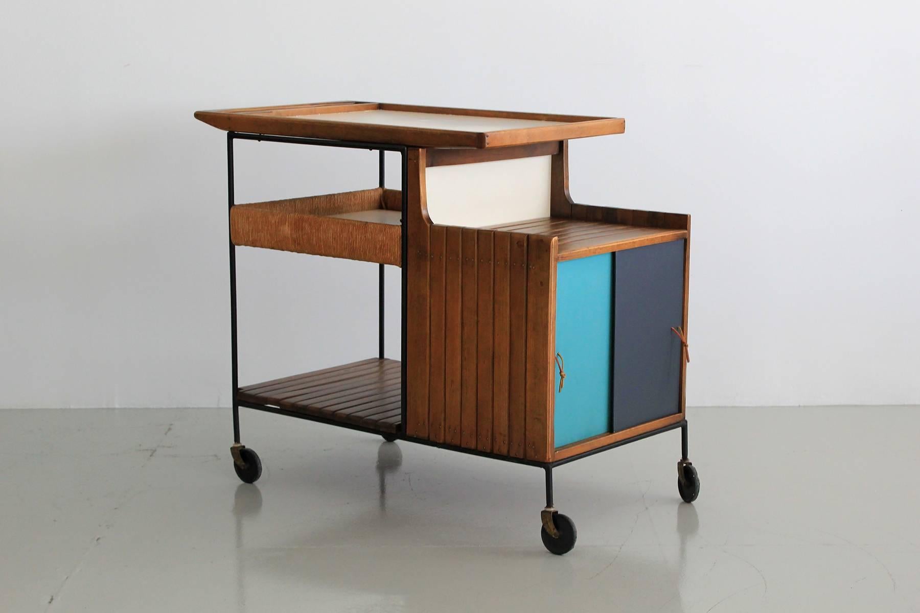 Great bar cart by Arthur Umanoff for Raymor. Black wrought iron frame, wood slat shelving, woven rushed storage compartment and sliding lacquered doors with extra storage. Great original vintage condition with original casters.