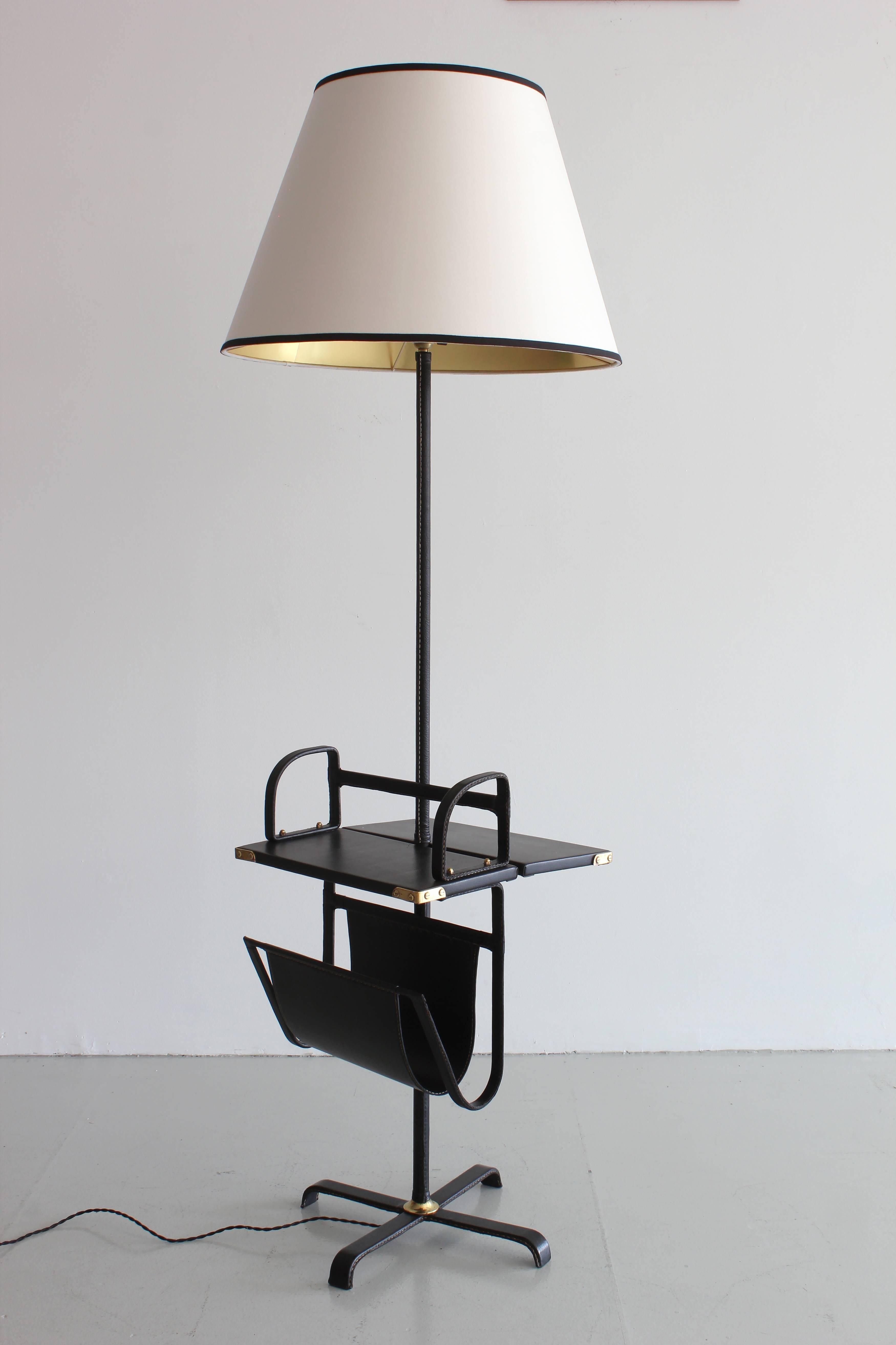 Exquisite floor lamp by Jacques Adnet with table and floating magazine holder, brass detailing and black leather.
  