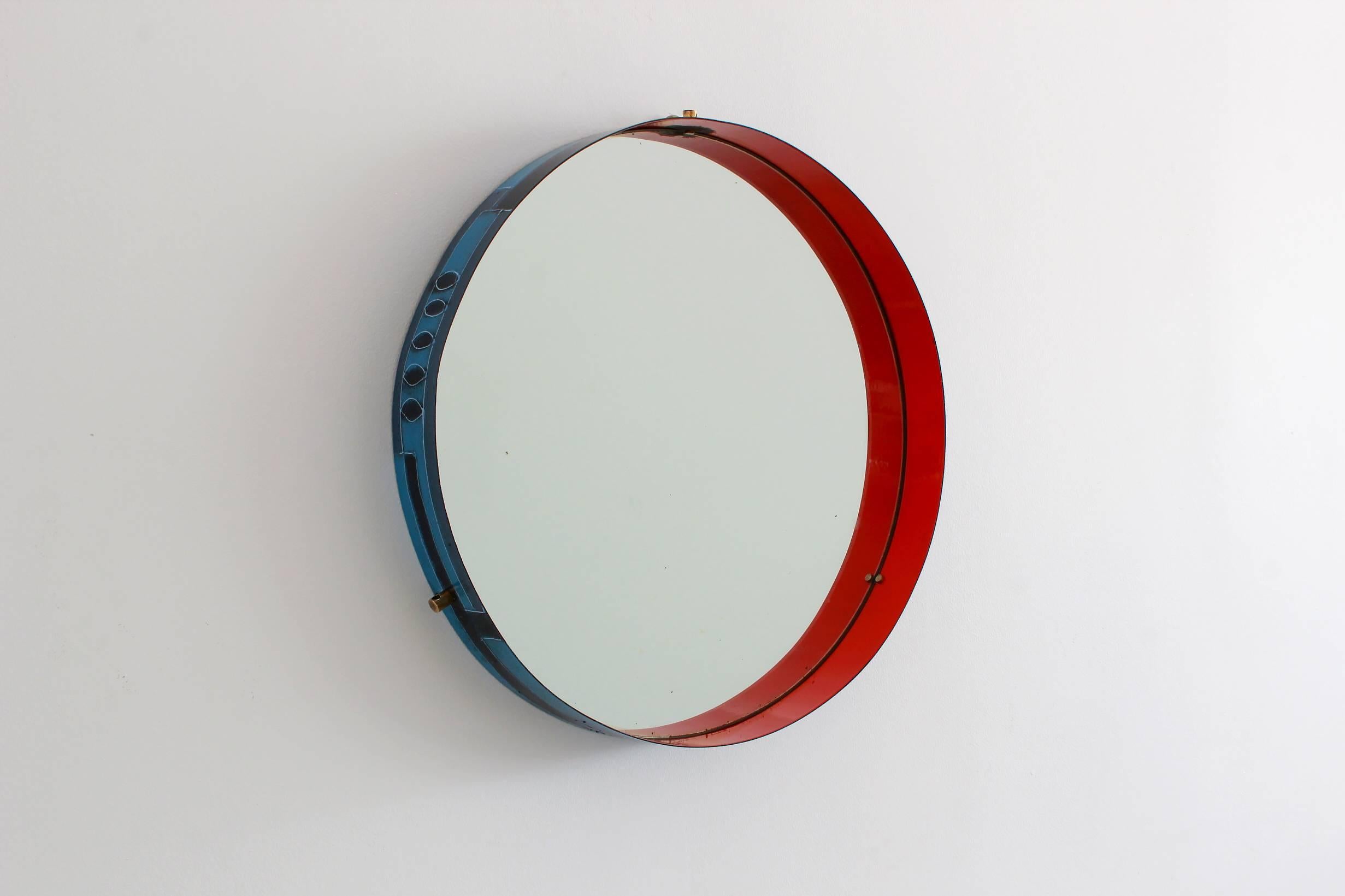 Stunning Italian circular wall mirror in blue and red ceramic on metal frame. Exterior of frame has painted shades of blue with leaf and geometric design. Interior is painted in a deep red lacquer. Amazing primary colors excite from all angles.