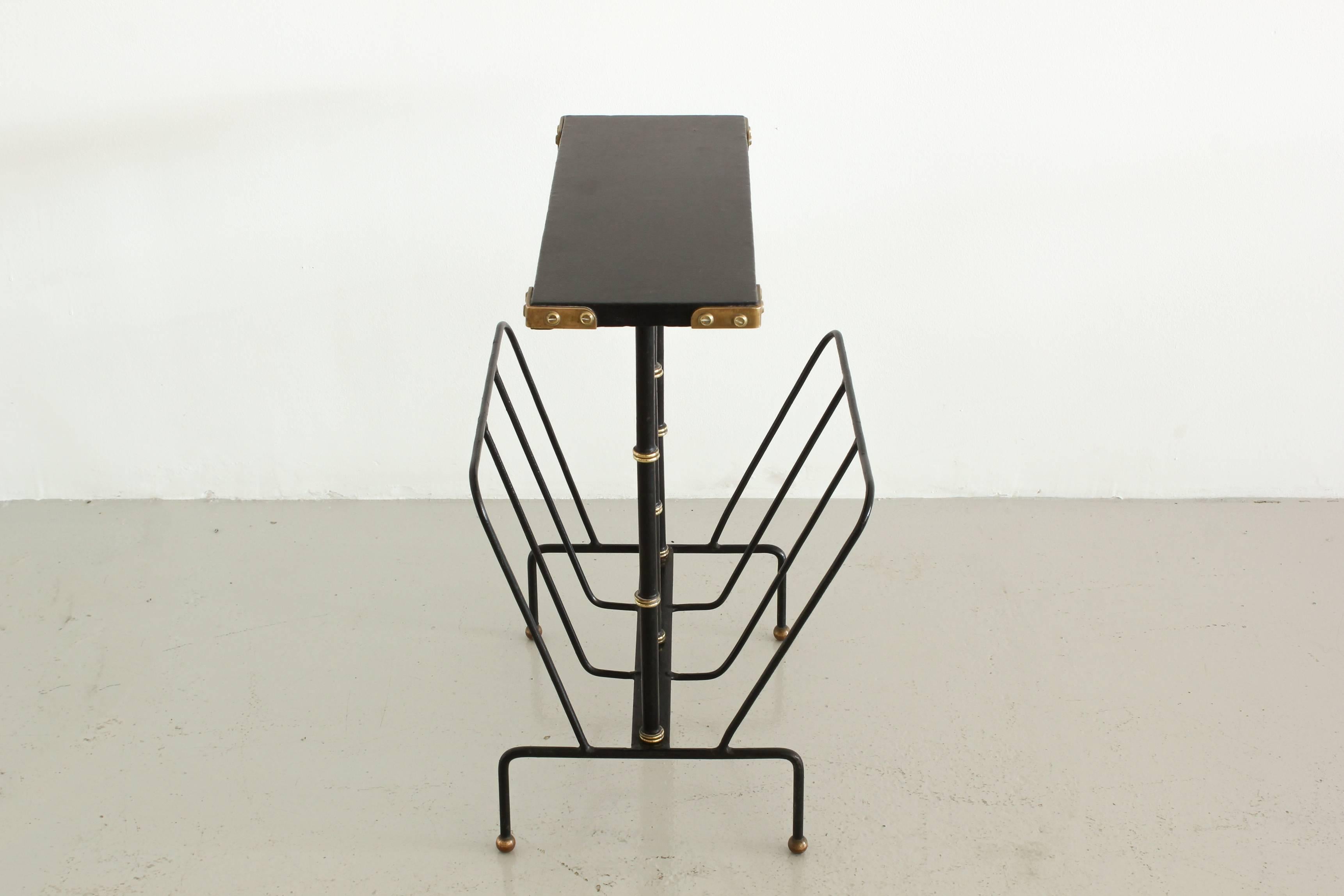 Handsome Jacques Adnet side table and magazine rack. Black leather top with brass corners rests on three iron and brass bamboo supports. Lower iron magazine rack on four leg iron base with brass ball feet. Stunning accent piece.
  