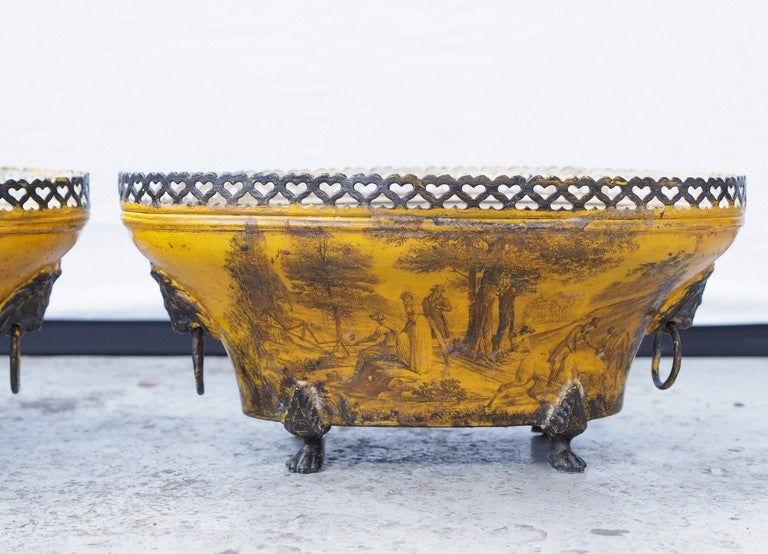 Pair of 19th century tole pierced work oval jardinière with yellow background and black scenic painting. Sitting on paw feet and having ringed lions head handles.