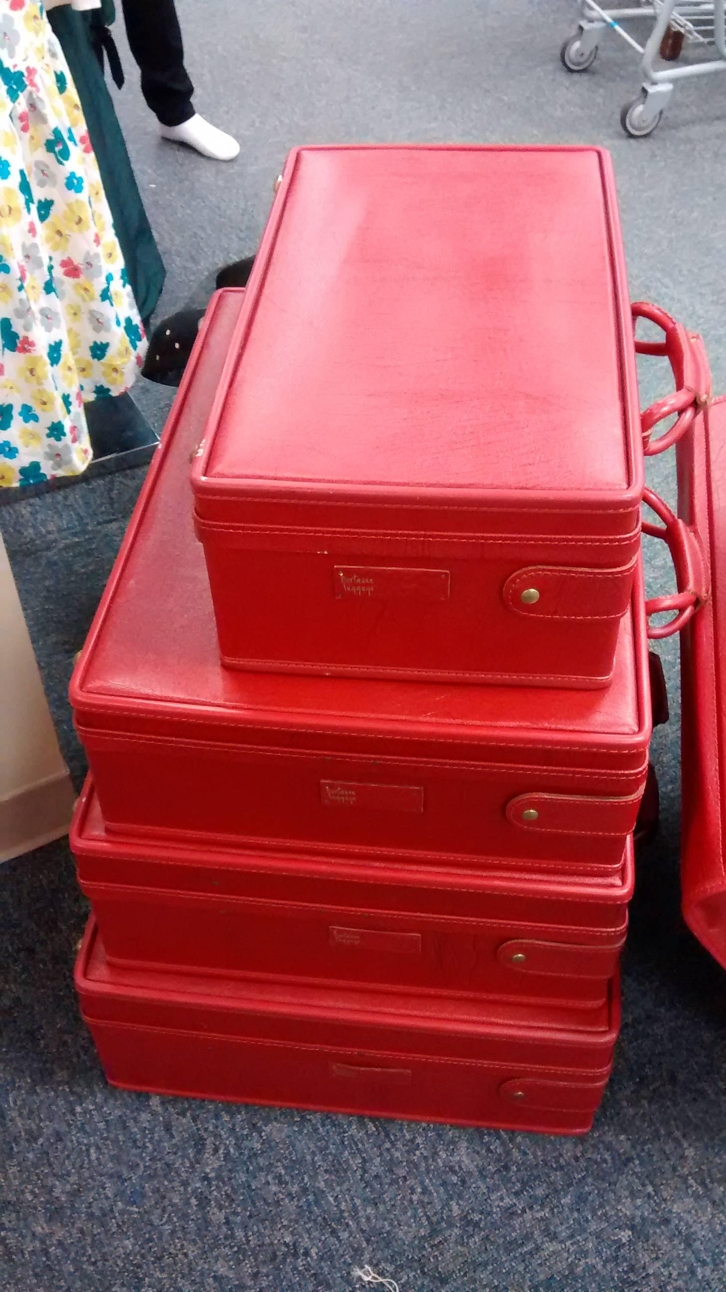 Fabulous find is this near mint condition set of barely used leather strapped Hartmann luggage, dating to the early 1960s. 

Done in a vibrant apple red, this set is comprised of four differently sized boxy suit cases and a hanging valise.