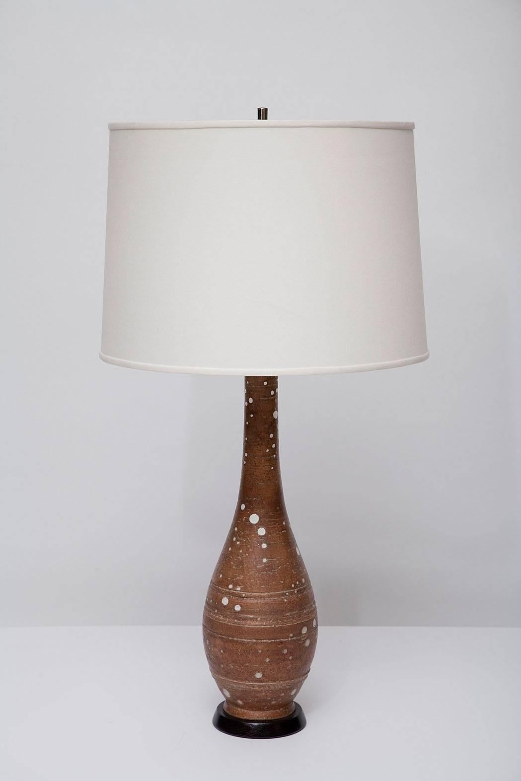 Brown stoneware lamp with random gloss-white glazed dots. Manufacturer's mark on underside. Black wood base, with new sockets and braided wiring. Measures: 28" H to top of socket. (Shade not included).
