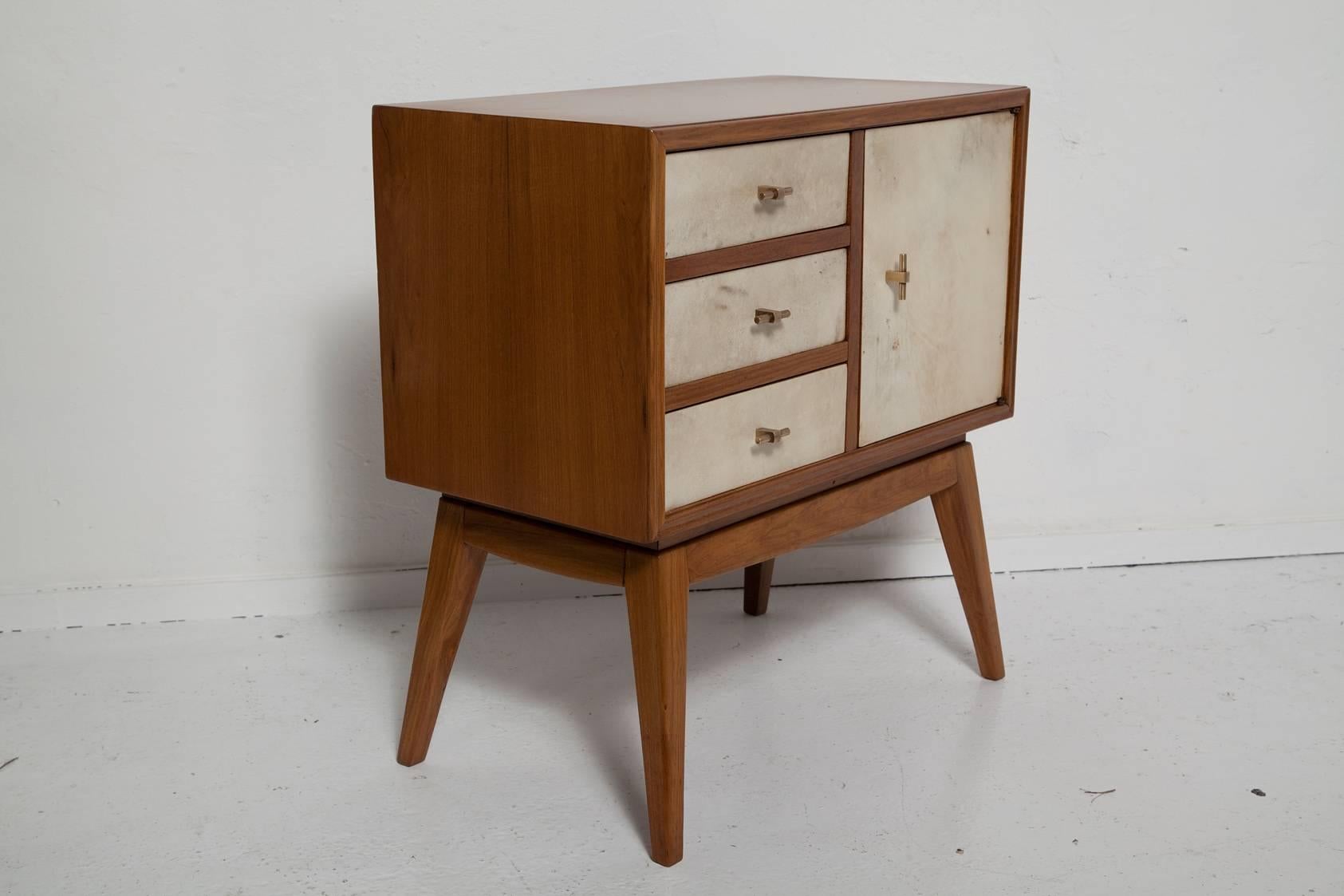 Charming, professionally restored and re-finished 1950s French night stands with teak wood frames, goatskin facing on drawers and doors, and solid brass T-pulls.