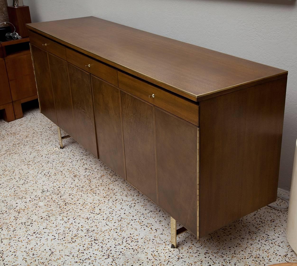Beautifully restored Irwin Collection brass trimmed mahogany credenza with leather door fronts and heavy flat bar brass legs by Paul McCobb for Calvin. Olive-tinged leather lined drawers and door fronts in excellent condition.