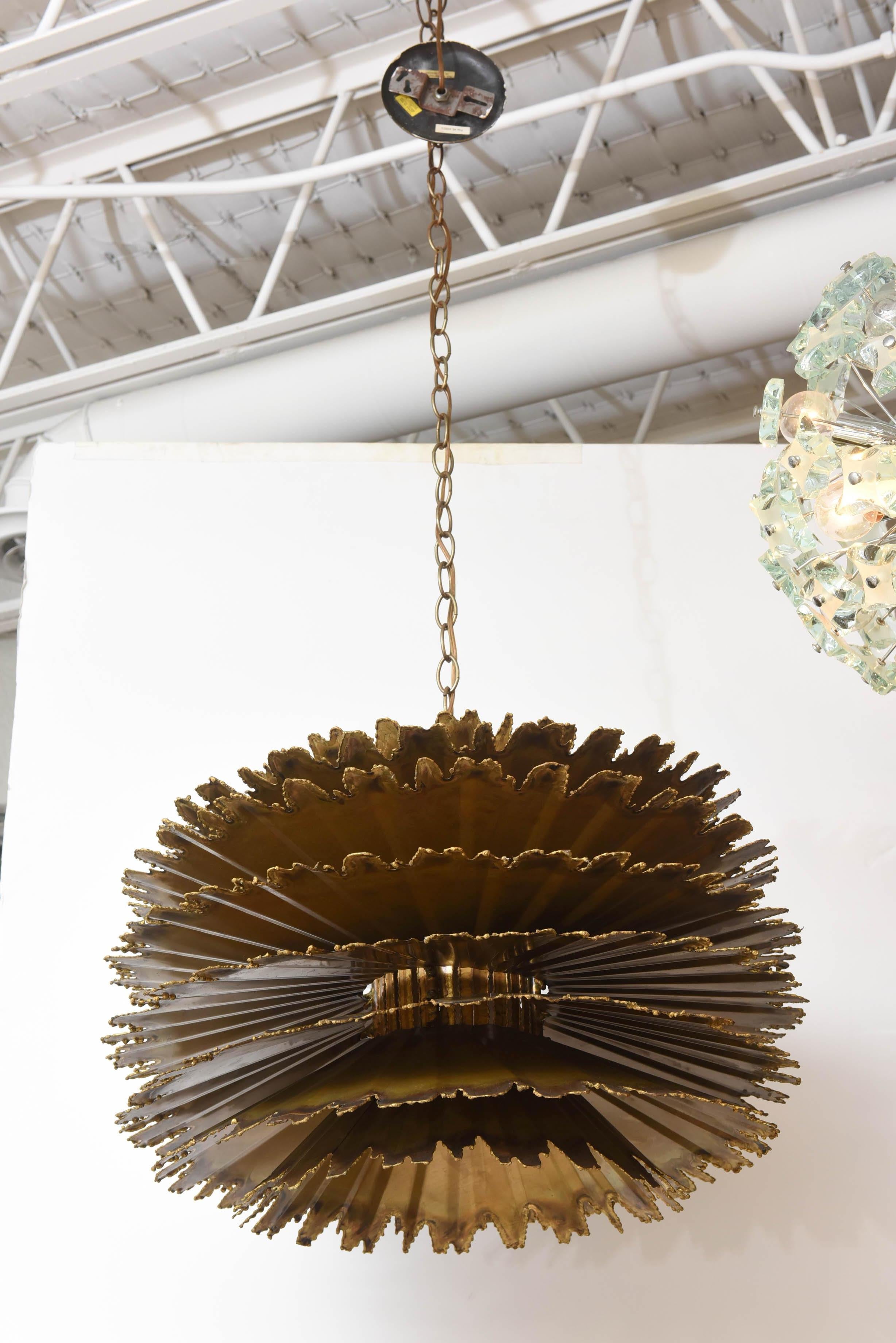 Ruffled layers of torch-cut brass create this stunning Brutalist orb chandelier, designed by Tom Greene for Feldman Lighting. Single socket, up to 150 watts. Height measurement below is for fixture only, and does not include ceiling canopy and