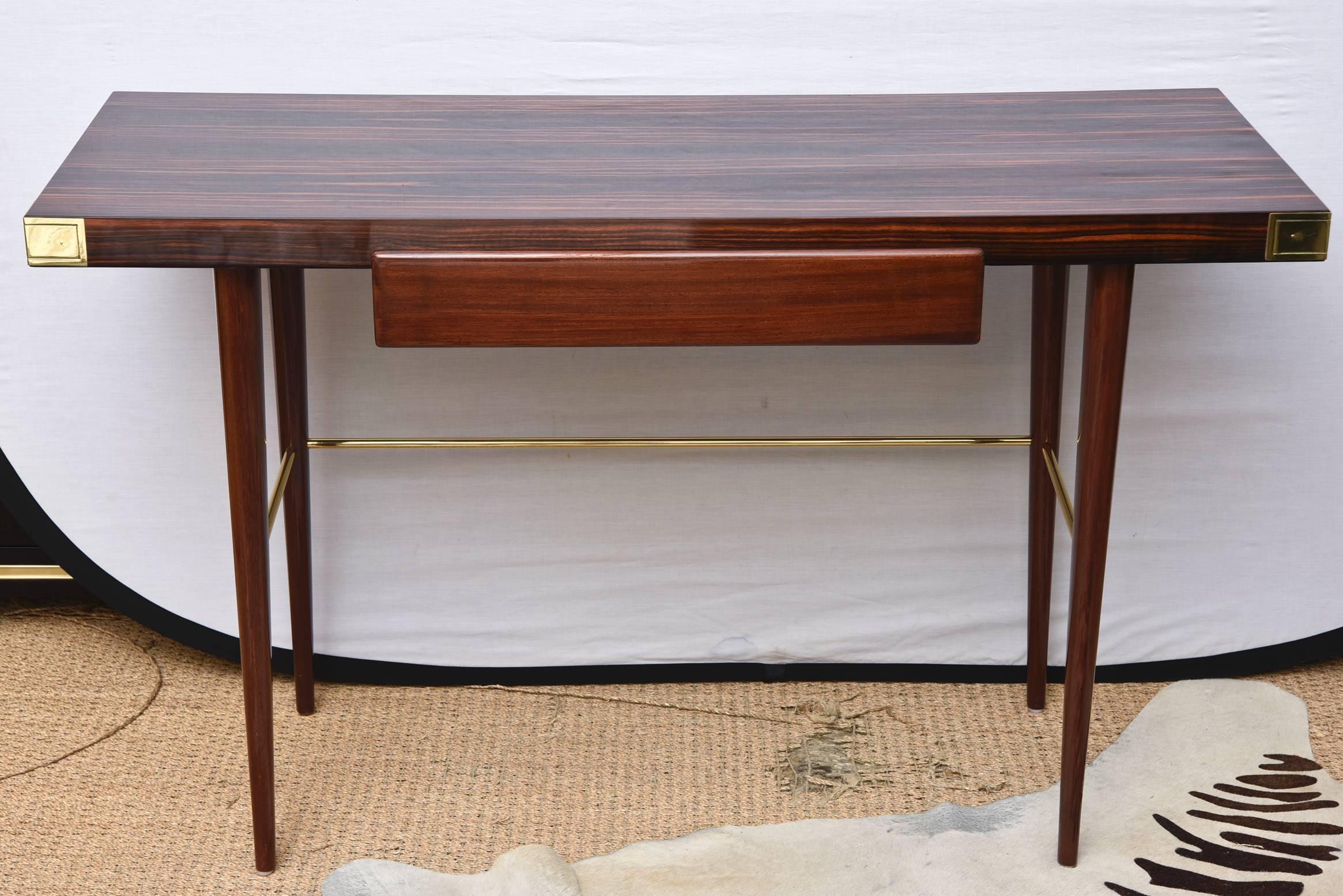 This sleek and fully restored Mid-Century Modern Walter Charak labeled desk and or writing desk for Tommi Parzinger is exquisite. The 4 polished brass corner tabs and brass stretcher on the bottom compliment the beautiful woods of Macassar ebony on