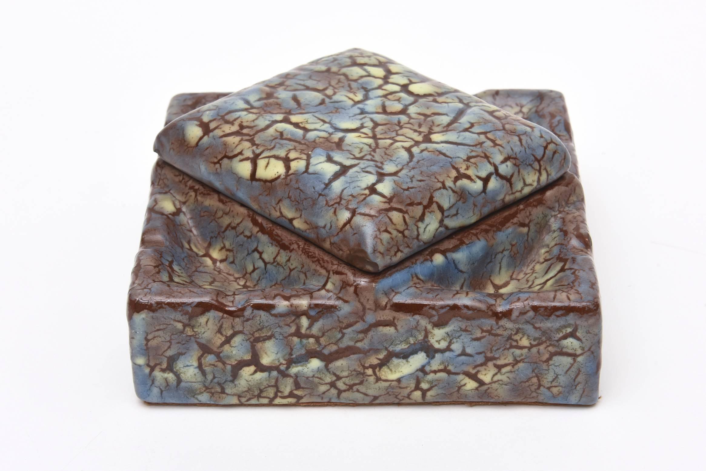 The mottled and crackled like design of the volcanic finish ceramic box looks very textural and dimensional. It is signed L.Dage, France.
The top is angled to give it an interesting asymmetrical look. This will make a great desk accessory an object