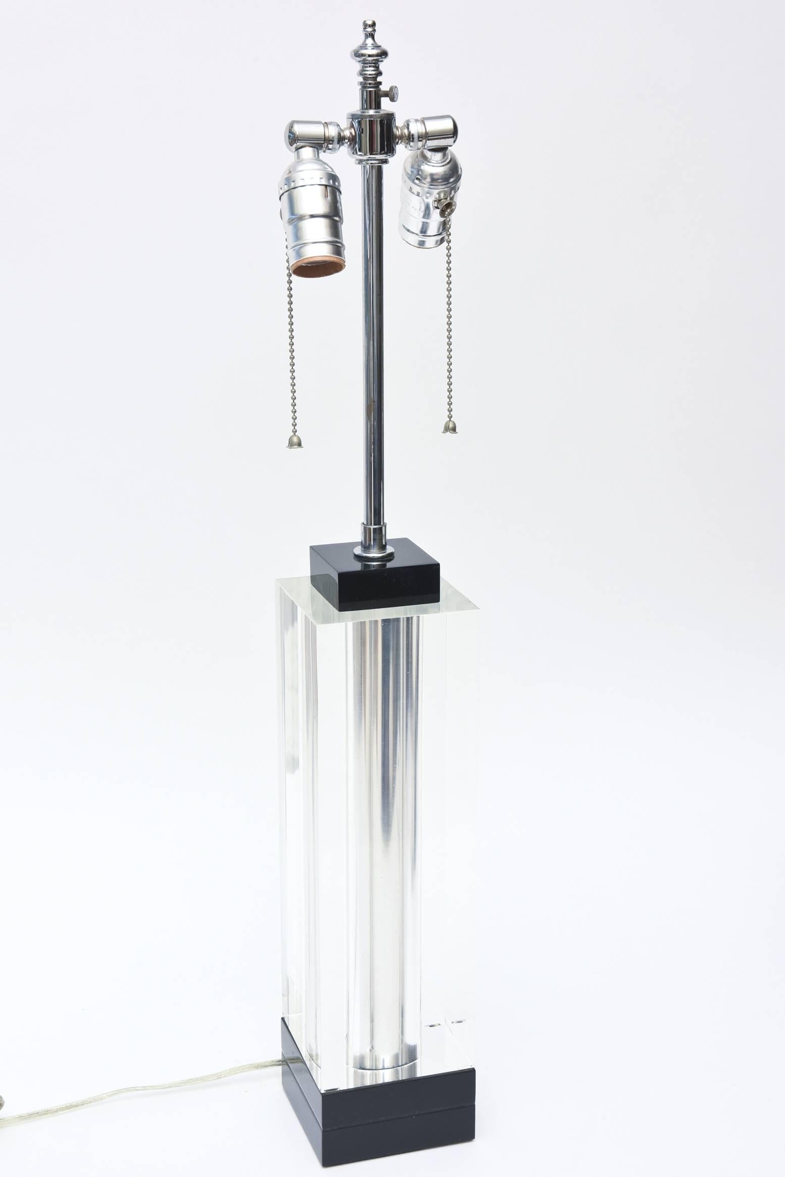 This handsome and modern square lucite lamp is clear in the center banded by a black lucite base and top. It has a polished steel column in the center that looks like it is floating. It is in excellent condition and makes for a sensational desk or