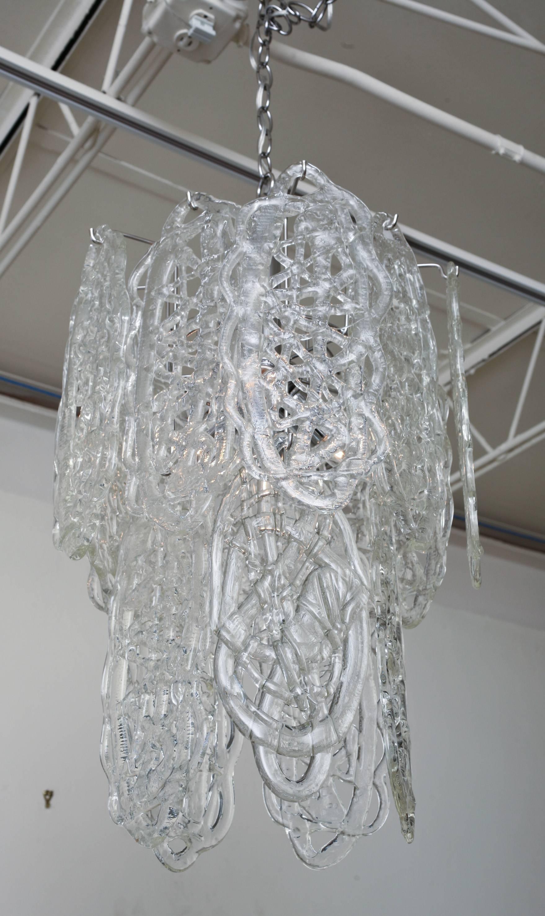 Questo splendido lampadario vintage Mazzega Murano è composto da 15 pendenti in vetro fuso bianco a forma di pretzel che creano un design e una forma astratti. La gabbia è stata interamente ricromata e la catena è di due piedi. I ciondoli sembrano