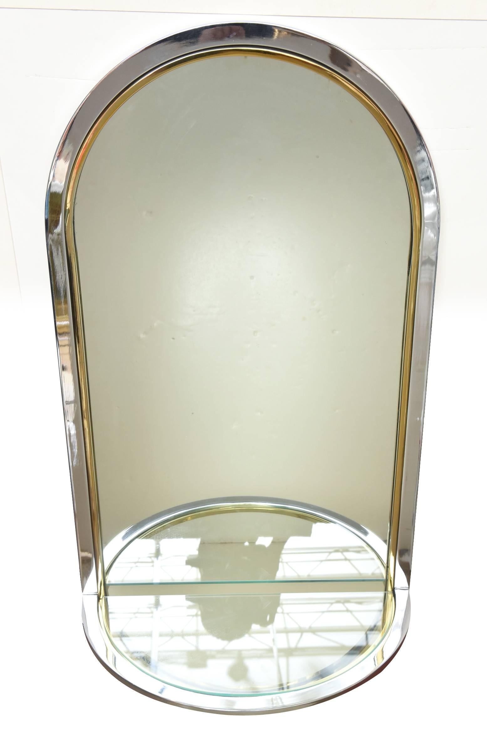 Ce merveilleux et polyvalent miroir mural arqué en métal de la Collection S Collective est doté d'une étagère en verre en forme de console. Il a été professionnellement poli et les matériaux utilisés sont le chrome à l'extérieur et la bande