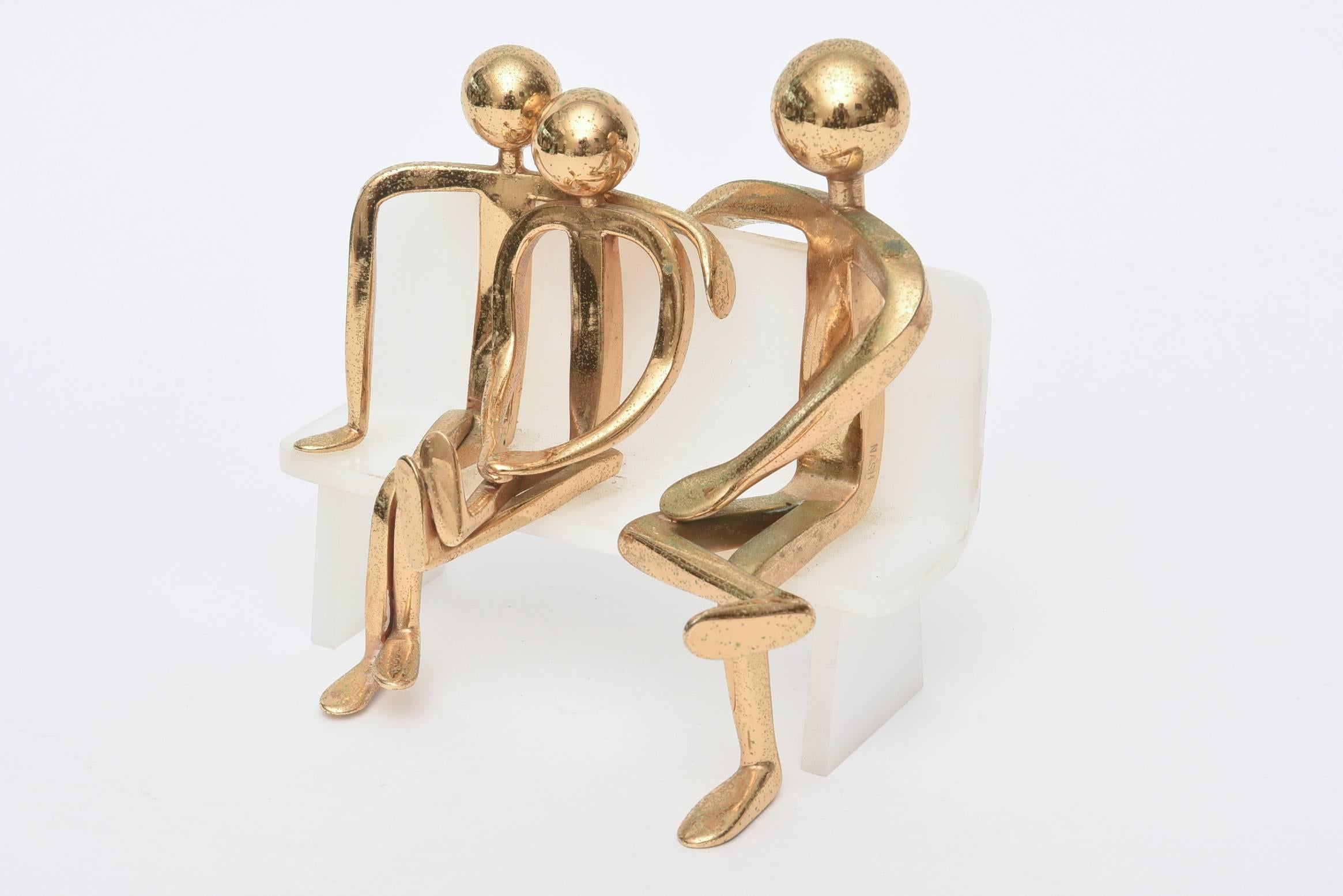 This whimsical and fun small sculpture of three modernist figures sit leisurely on a white Lucite bench. They are attached with gold-plated pins/screws.
They are gold-plated over brass and it is signed by Nash.