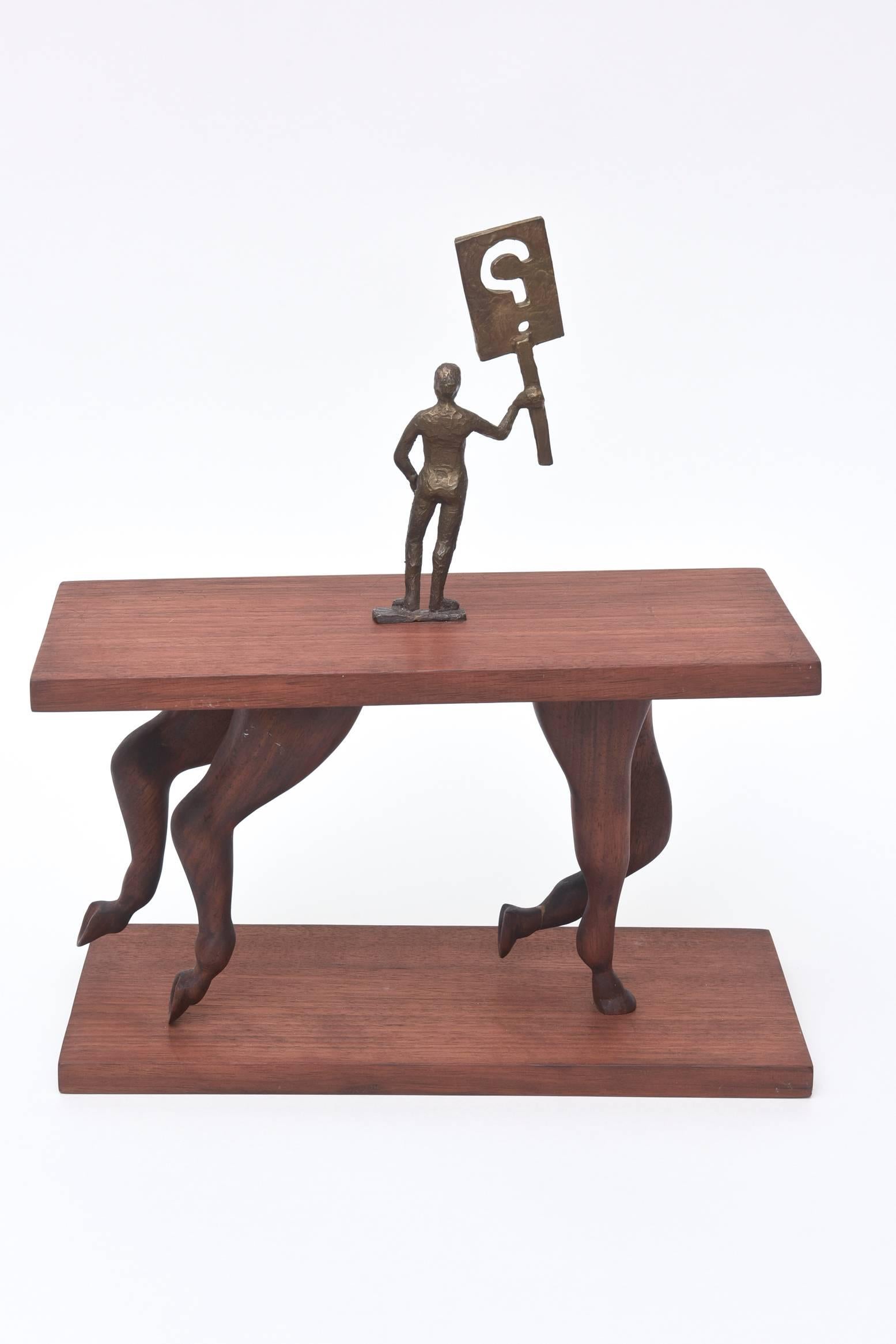 This more contemporary sculpture is dated 06 and the signature is hard to read but the initials are RW. It is one of a kind. The wood looks like walnut and the man holding the question sign is bronze. The horse legs in a gallop pose raise the