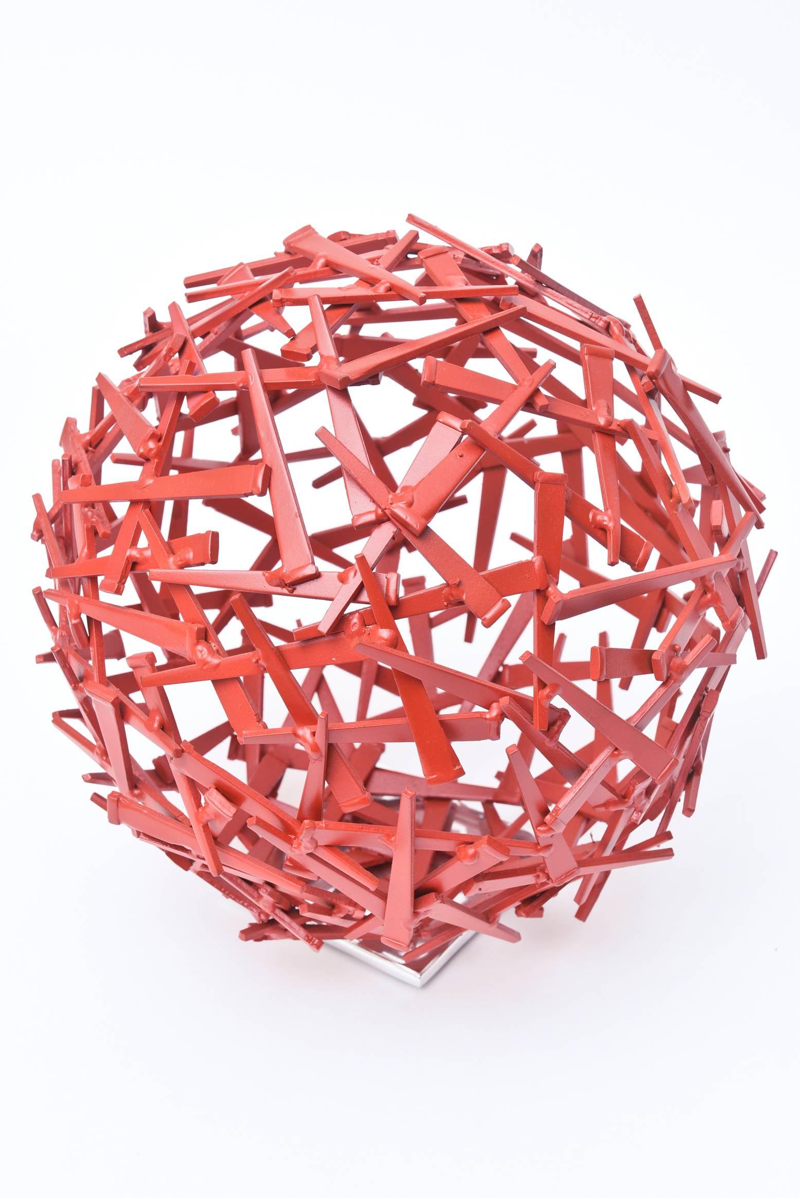 This dynamic wonderful globe like sphere sculpture has juxtaposed cement nails that are all paprika red enamel over steel going in abstract different directions. It sits on square chrome plated base. It is a limited edition sculpture by Glen Mayo.