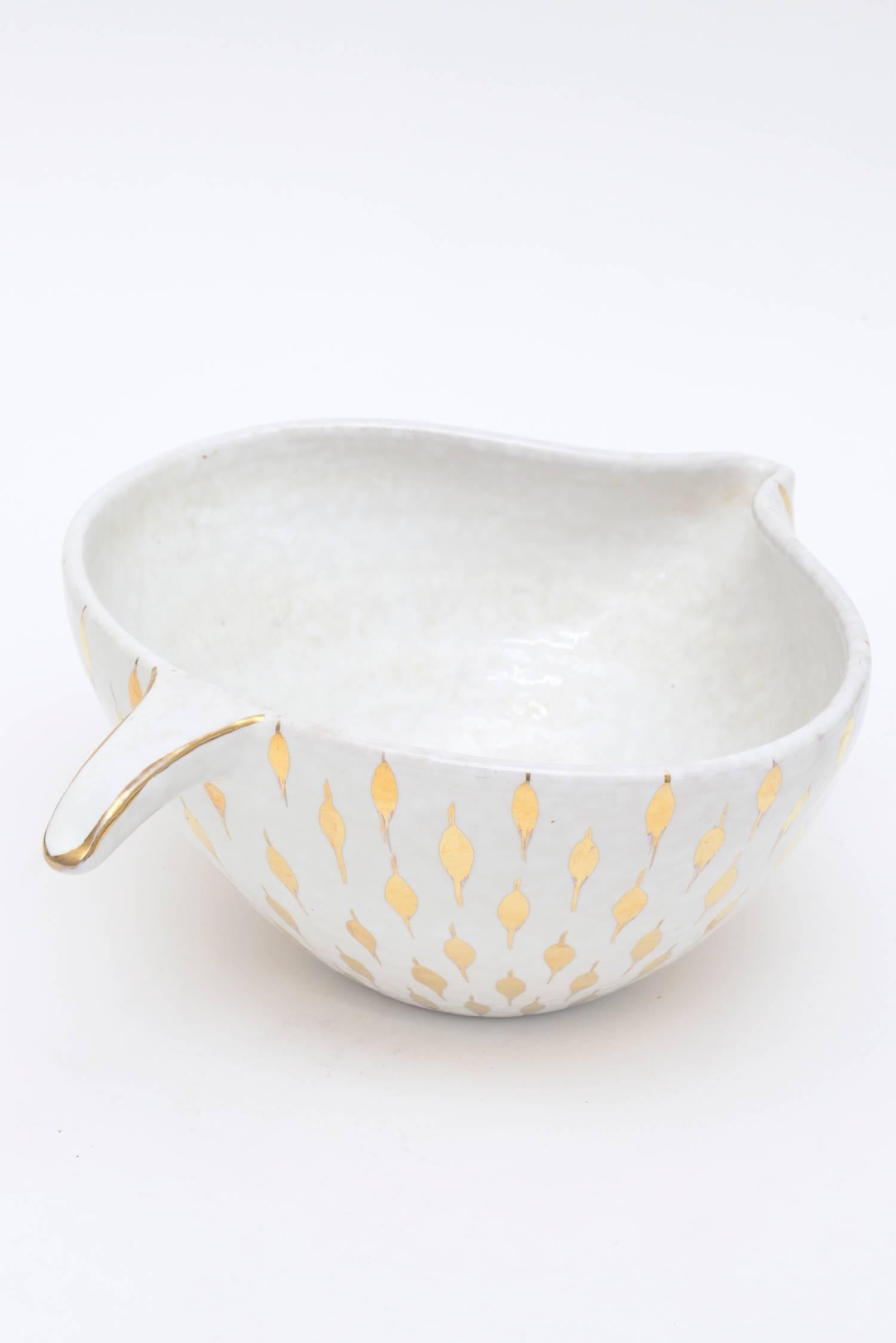 This sculptural vintage Italian Aldo Londi for Bitossi ceramic bowl or vessel has gold painted teardrop like surround shapes on the exterior over white ceramic with a short sculptural handle. It is called the feather plume. The shape is organic with