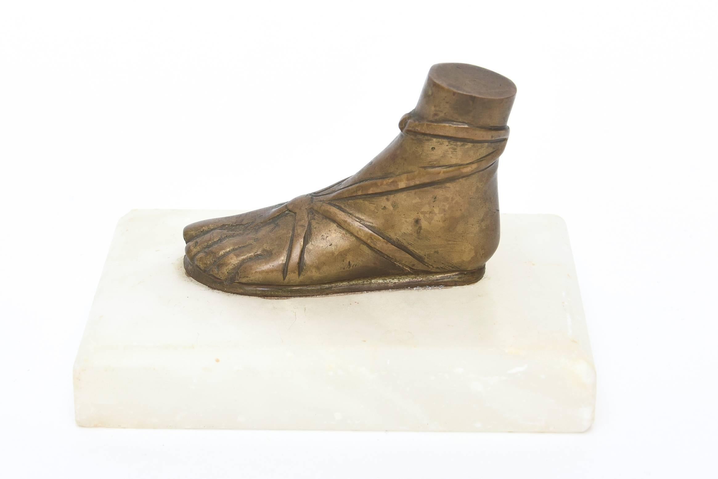 This Fornsetti style vintage paperweight, sculpture and desk accessory has a patinated bronze roman foot atop a white marble base. The bronze has been slightly polished, it is as is with a lovely patina on it. It was imported for Saks Fifth Avenue
