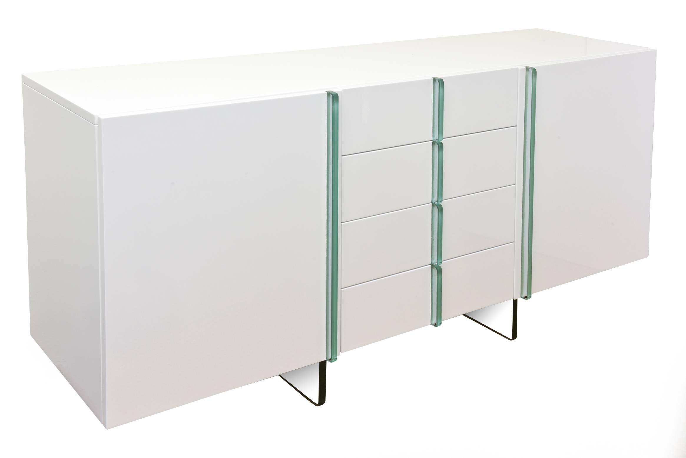 This chic combination of white lacquer over wood and green glass is fresh and clean in this cabinet/ buffet and or console. It has been newly restored.
It has glass drawer pulls and the square bases are glass. It is a great size for most