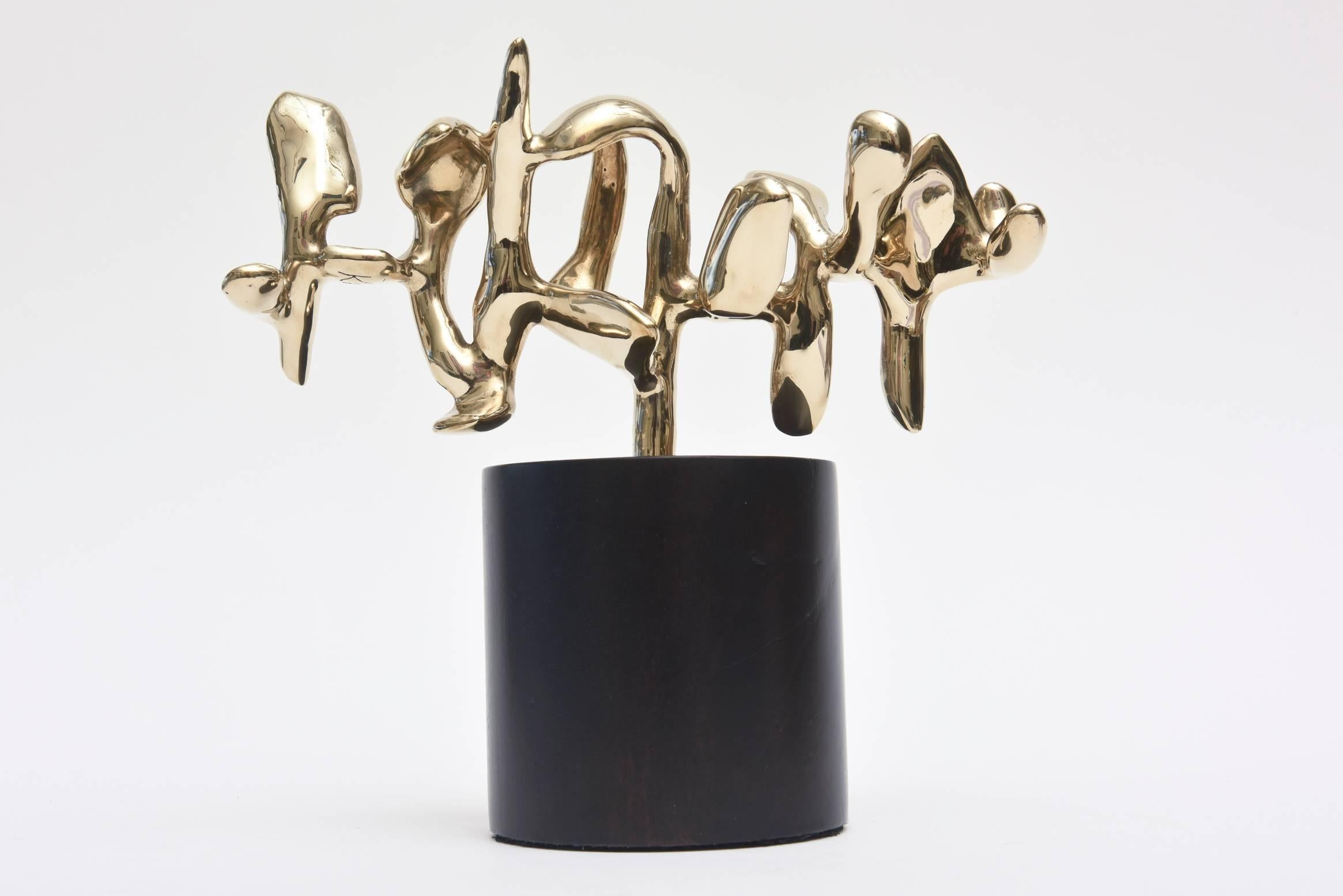 This polished bronze sculpture is on an ebonized wood base is by Eli Karpel, a NY artist. It is signed and of a very small edition. It is a continuum of abstract figures and forms in undulating sequence. The height of the sculpture varies as there