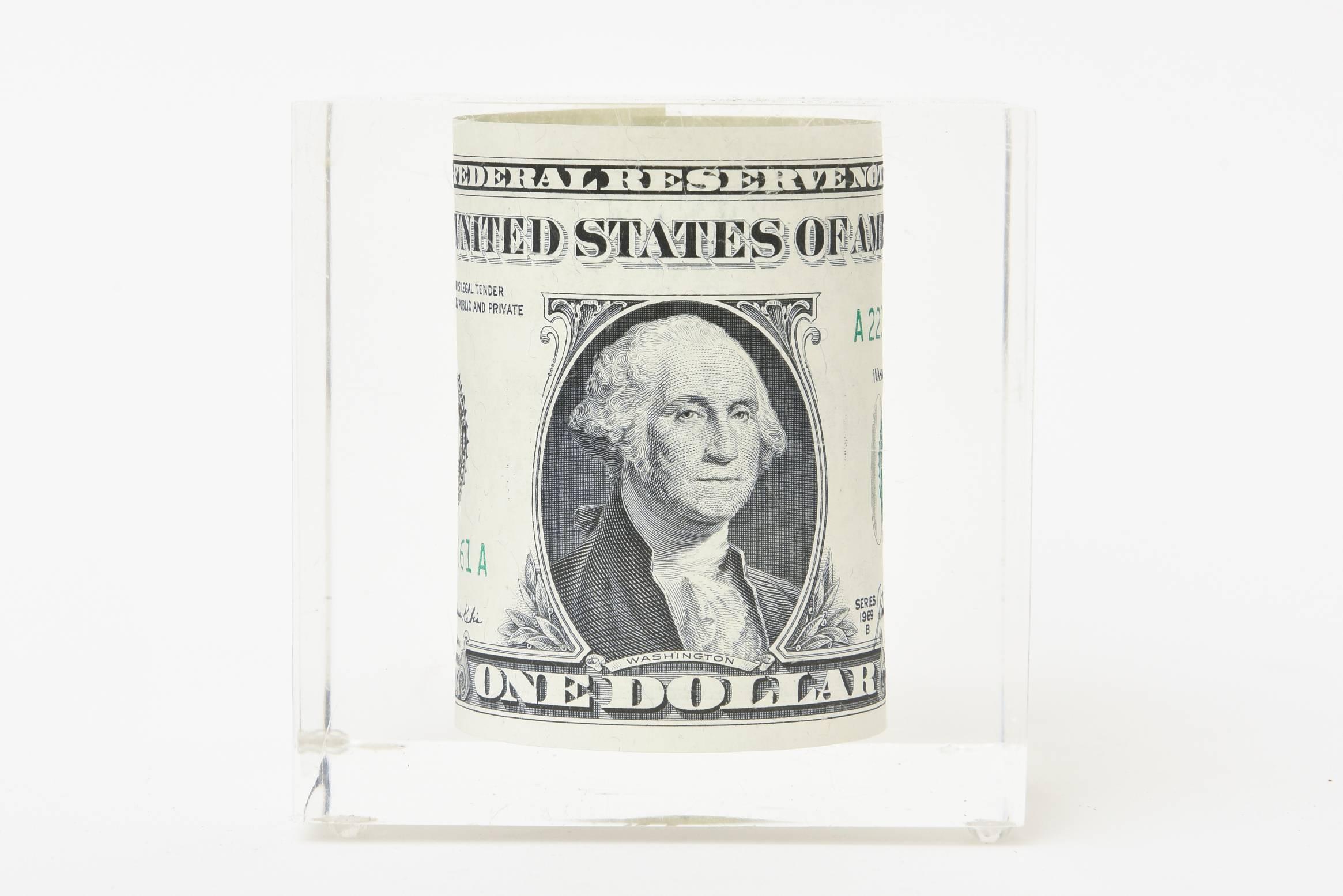 This fun and vintage rolled dollar bill is encased and floating in lucite. A great desk accessory sculpture or a paperweight. Always whimsical and conversational. It is from the 1970s.

  