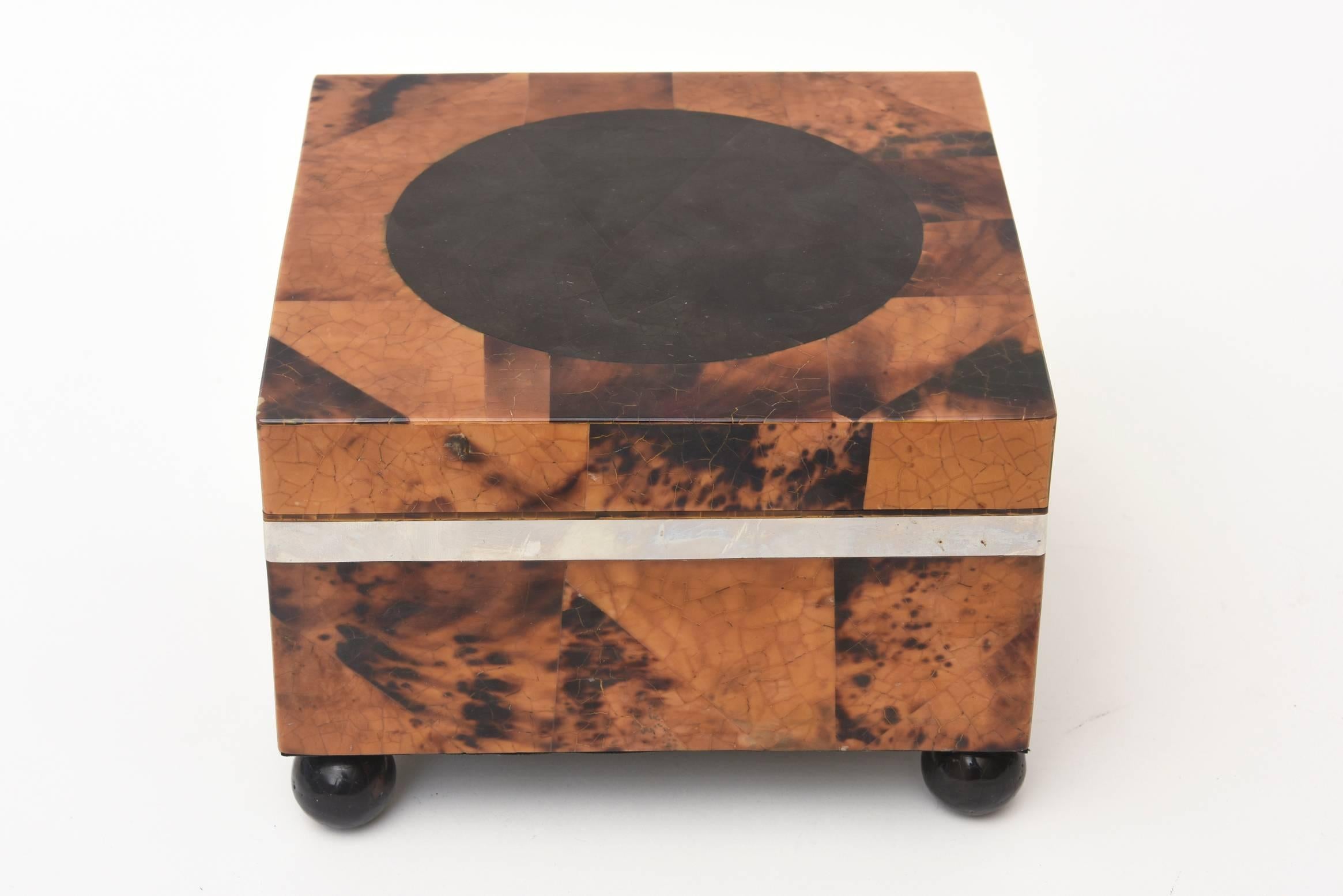 This lovely and unusual hinged square box by Maitland -Smith with four black lacquered wood ball feet is tessellated tortoise shell. It has a black velvet lining. The chrome applied banding is to the top of where the box would open. This is perfect