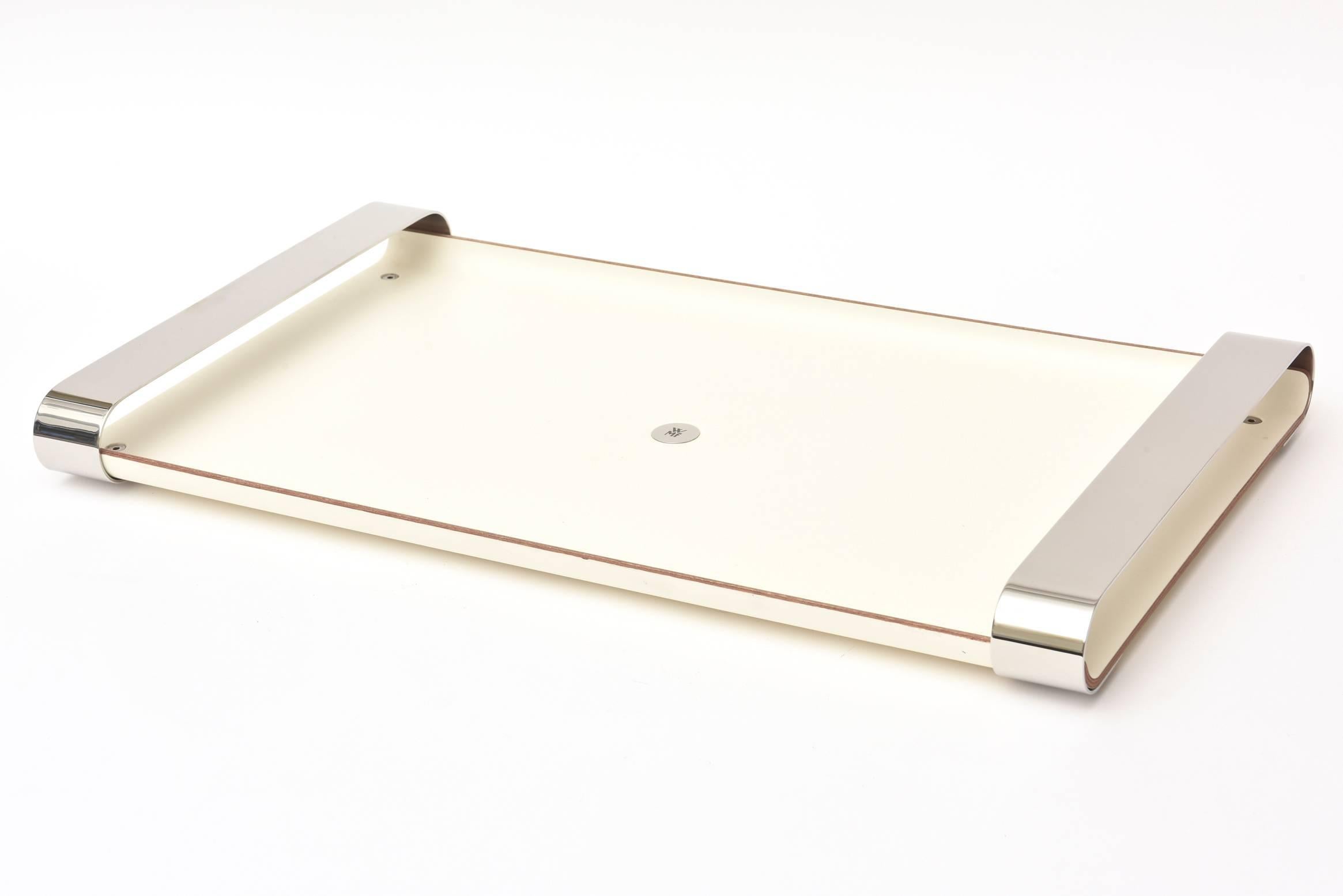 This handsome and versatile rectangle modern tray or barware tray is by the infamous and well know German company called WMF is simple and elegant.
It is off-white laminated wood with the insignia of WMF in the center of stainless steel.
It has