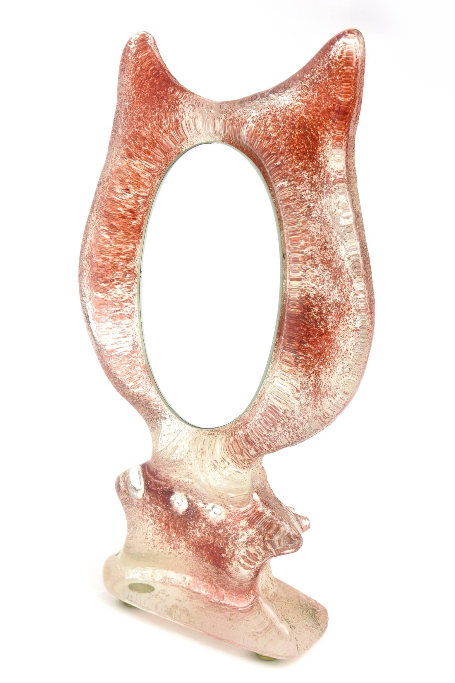 This charming small glass Kosta Boda attributed tabletop mirror in the shape of a cat's ears has the French glass technique of the look of patte de verre but is sandblasted glass. The colors are in hues of orange/rust red and clear glass. It is