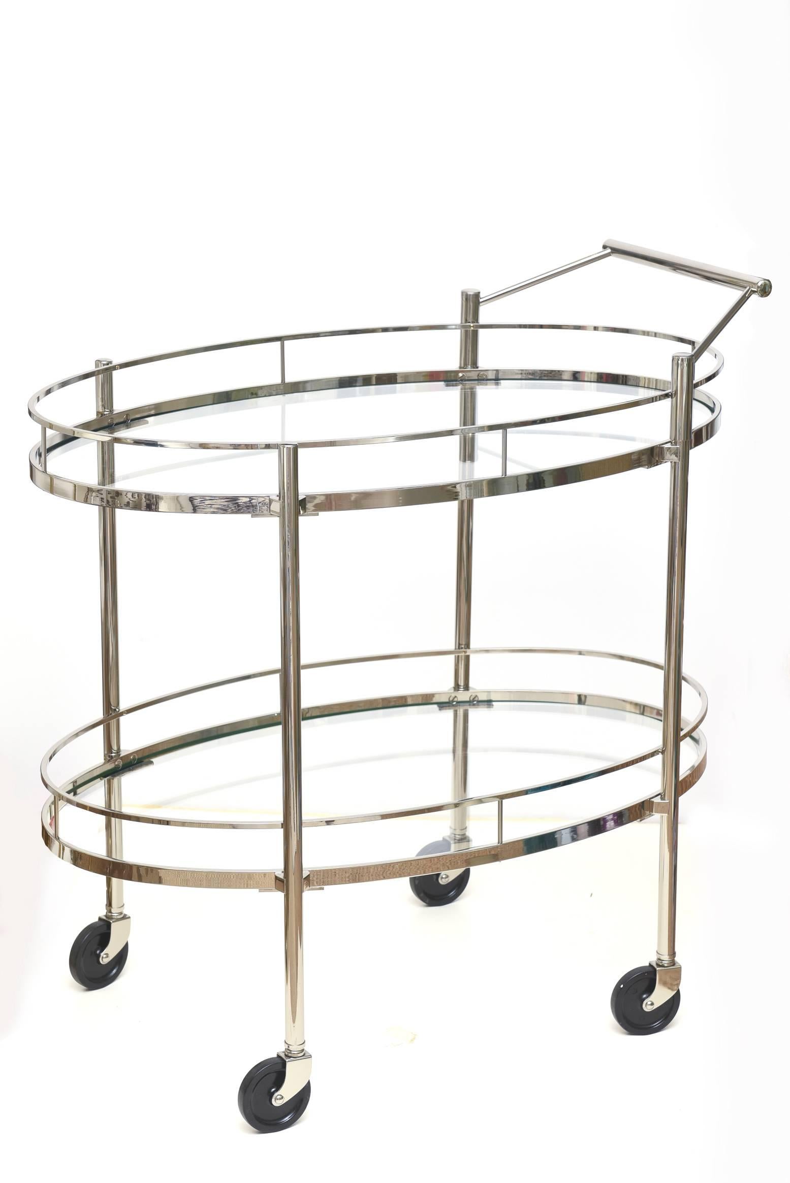 This midcentury oval two-tiered bar cart or trolley signed Maxwell-Phillips NY has been newly restored with nickel silver over brass. The wheels are original to the cart/trolley. The glass has not been replaced. It looks modern yet is from the