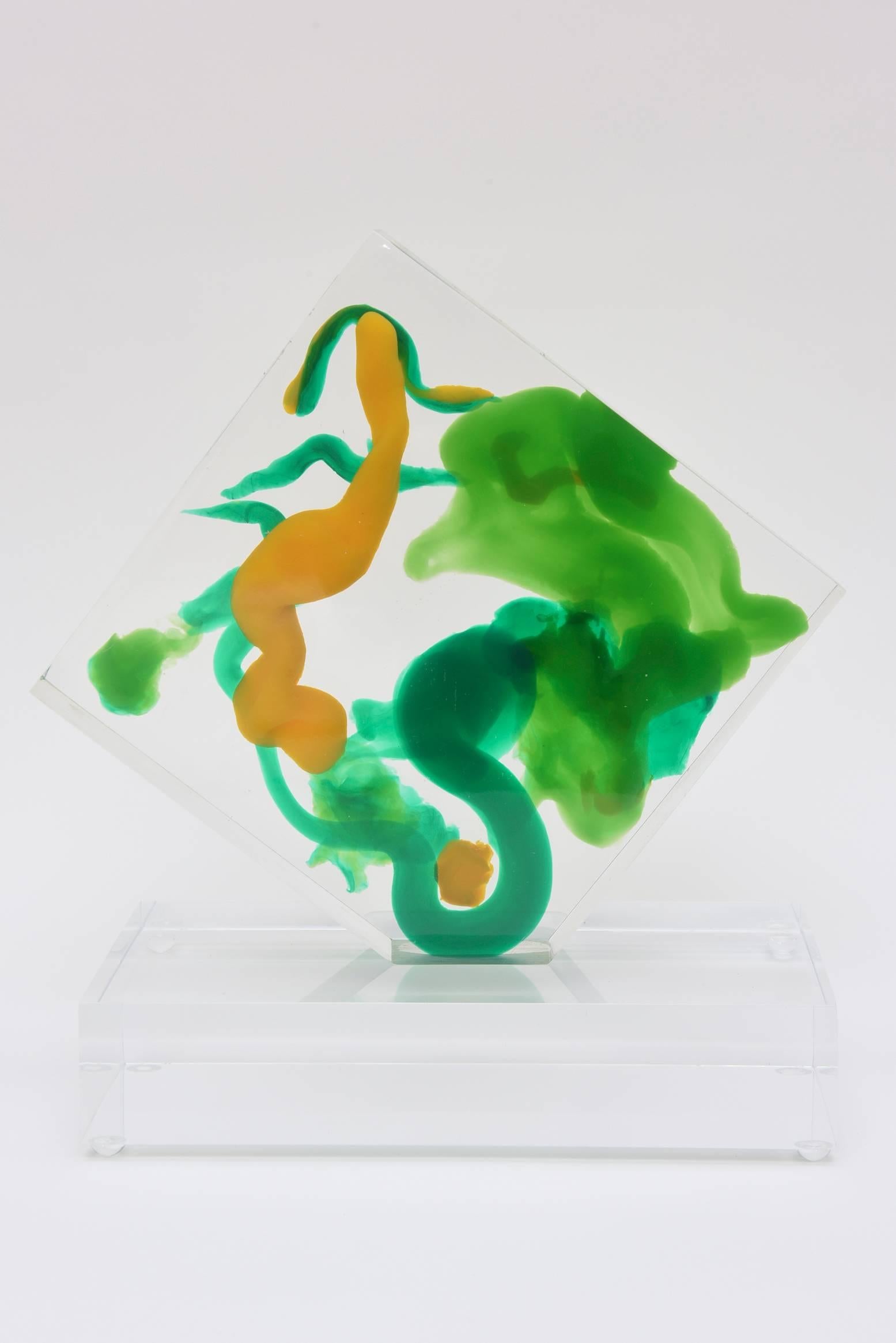 Abstractions of floating emerald shades of greens and tans become abstract blobs in this embedded fluid Lucite sculpture. It is if a painting is inside of the Lucite. The abstract colored designs seem to float in the inside space of the clear