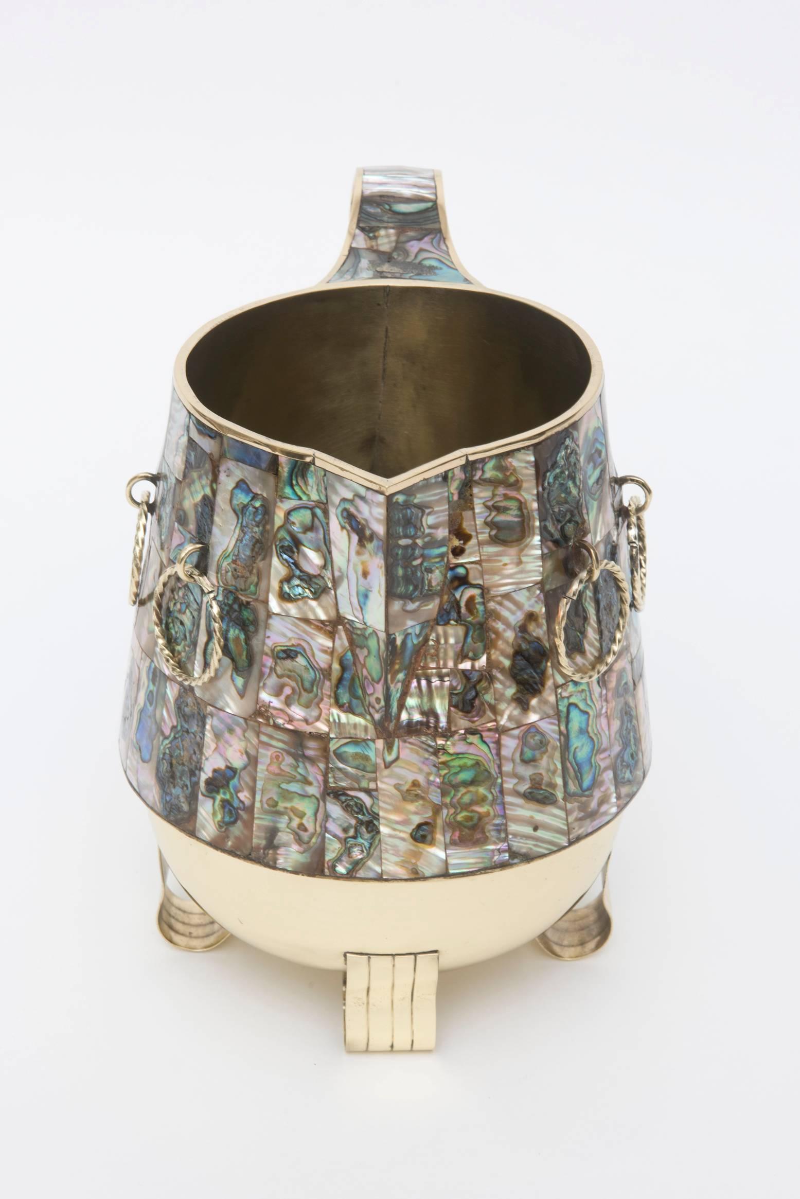 This wonderful combination of abalone and polished brass pitcher or vase, vessel or object is signed on the bottom Hecho En Mexico. It is vintage and has the look of the lined Tommi Parzinger style on the modern feet. The 6 brass roped rings