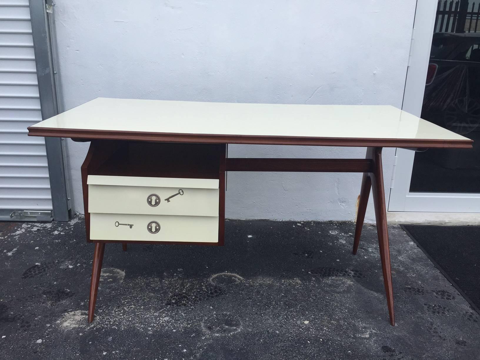 Reminiscent of Fornasetti's work, this attractive and functional desk is adorned with Keys and locks to the front and back. Top is lacquered beige and the desk frame in natural walnut finish. Scissor style legs and two drawers, slide out shelf, and