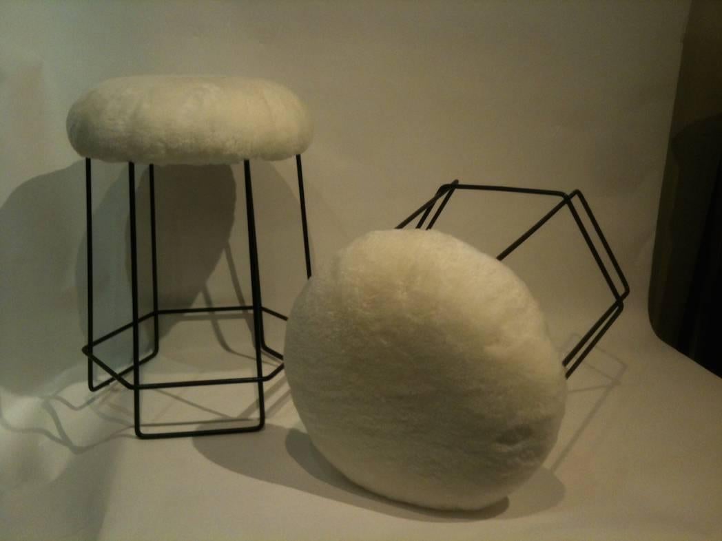 A set of three stools each featuring bases in black steel wire, each which supports a round seat. Each seat has all new upholstery done in a creamy, natural shearling. In the style of Jean Royere, France circa 1955.
