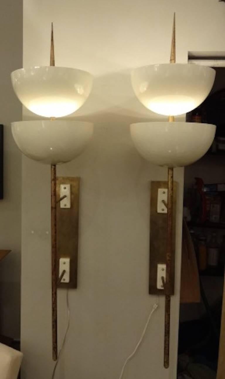 A pair of rare grand scaled Mid-Century wall sconces each featuring pole shaped bodies in brass with double arm wall supports and two large bowl shaped uplight cream lacquered shades, each bowl with two interior light sources. There has been an