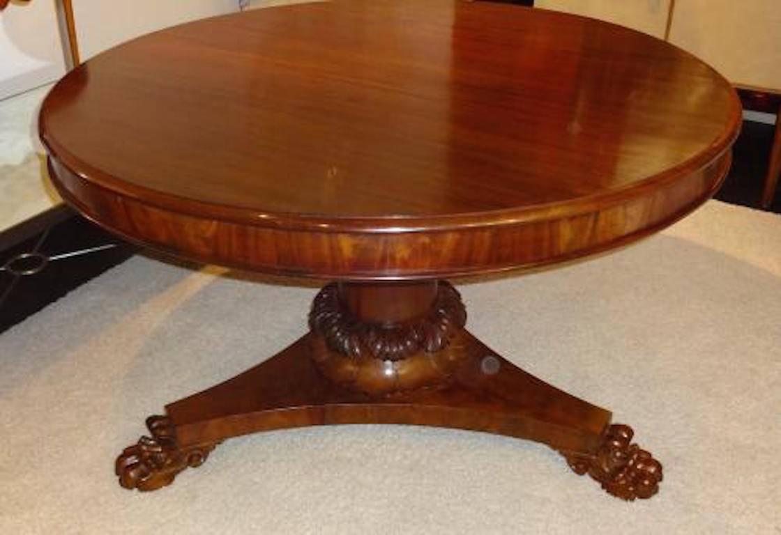 A mid-19th century antique center or breakfast pedestal table in mahogany featuring a round top with deep skirt, a tapering center pedestal with acanthus leaf decoration and a tripod shaped base with carved lion paw feet. The table has been fully