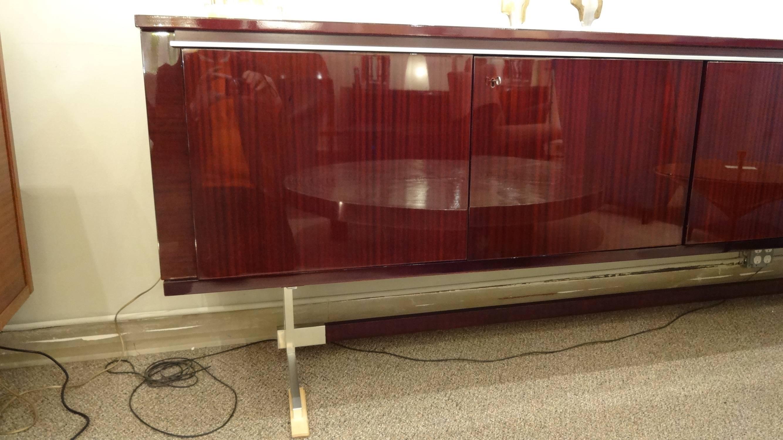 A modernist sideboard featuring a body in polished rosewood with four doors and a band of aluminum running just below the pieces top which is used as the doors handles. The body of the sideboard is supported by a double pedestal modernist base in