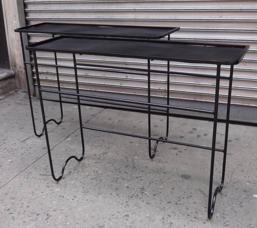 A rare pair of Mid-Century consoles in matte black painted wrought iron. Each featuring side leg supports with a convex shaped foot and three stretches. The consoles also feature Mategot's classic pierced metal tops with solid frames. Fully