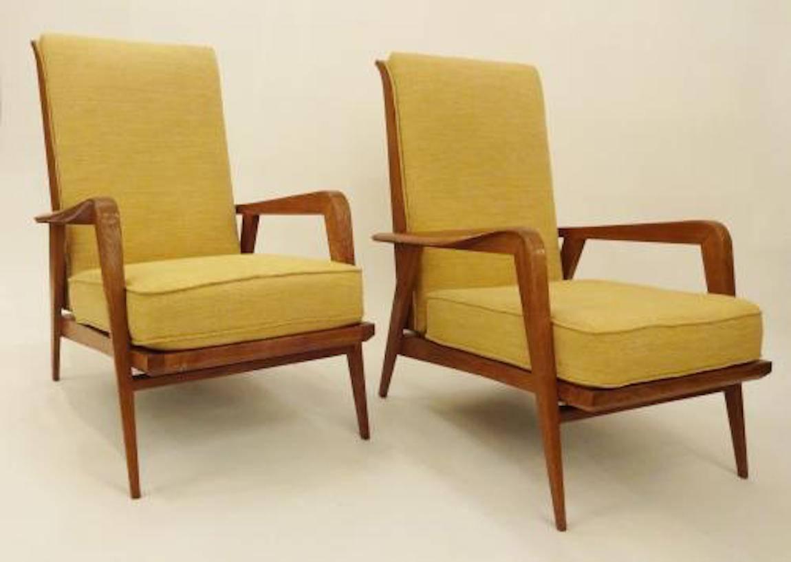 Pair of modernist lounge chairs each featuring frames in waxed oak with curving carved armrests, splayed tapering legs, a tight back and loose seat cushion. The backs of the chairs recline and are adjustable and can be positioned in multiple