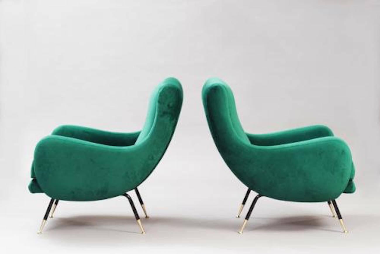 Pair of Mid-Century club chairs each featuring rounded bodies with integrated armrests and loose seat cushions. The clubs also feature splayed black lacquered steel legs with brass sabots and rounded brass feet. The clubs have all new upholstery