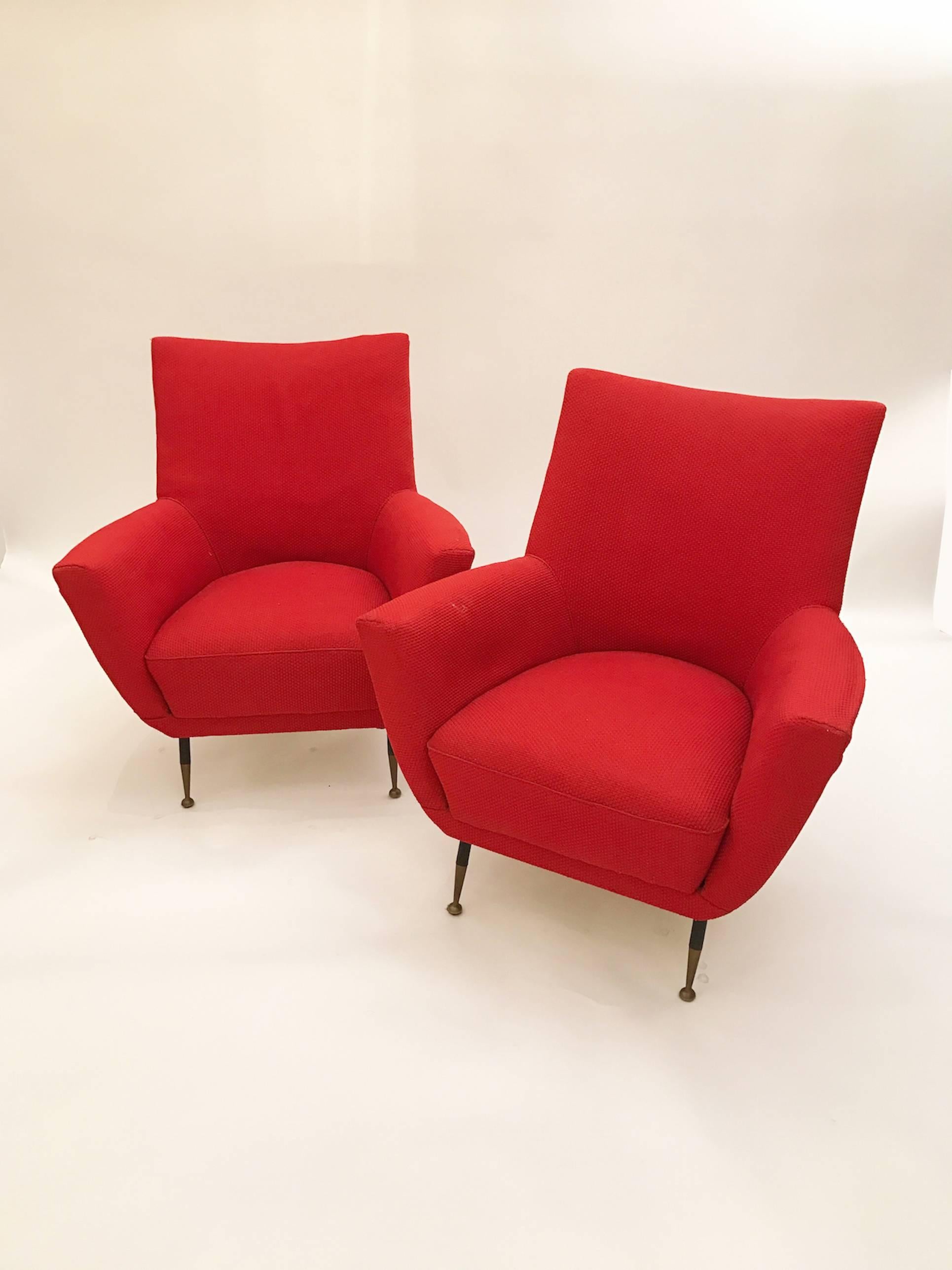 Pair of Mid-Century club chairs each featuring tight seats and backs with integrated curving armrests and tapering blackened steel legs with brass feet. The clubs are upholstered in their original red textured fabric. There is a matching settee that