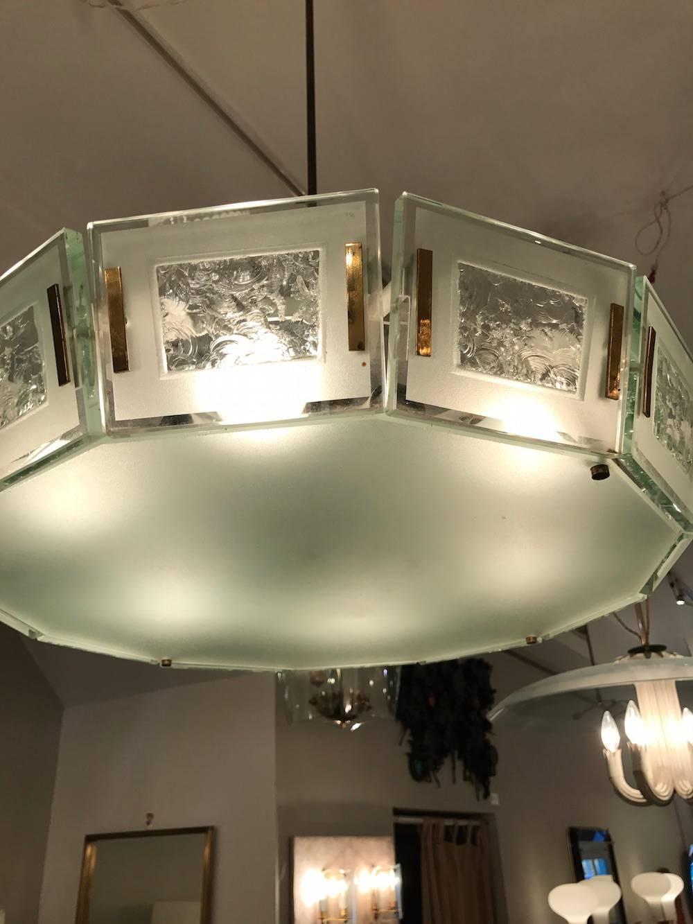 Mid-Century chandelier featuring a brass structure with twelve interior light sources as well as a faceted diffuser, surrounded by frosted and chiseled rectangular glass panels, suspended from a rod and canopy, circa 1963. Fontana Arte model number