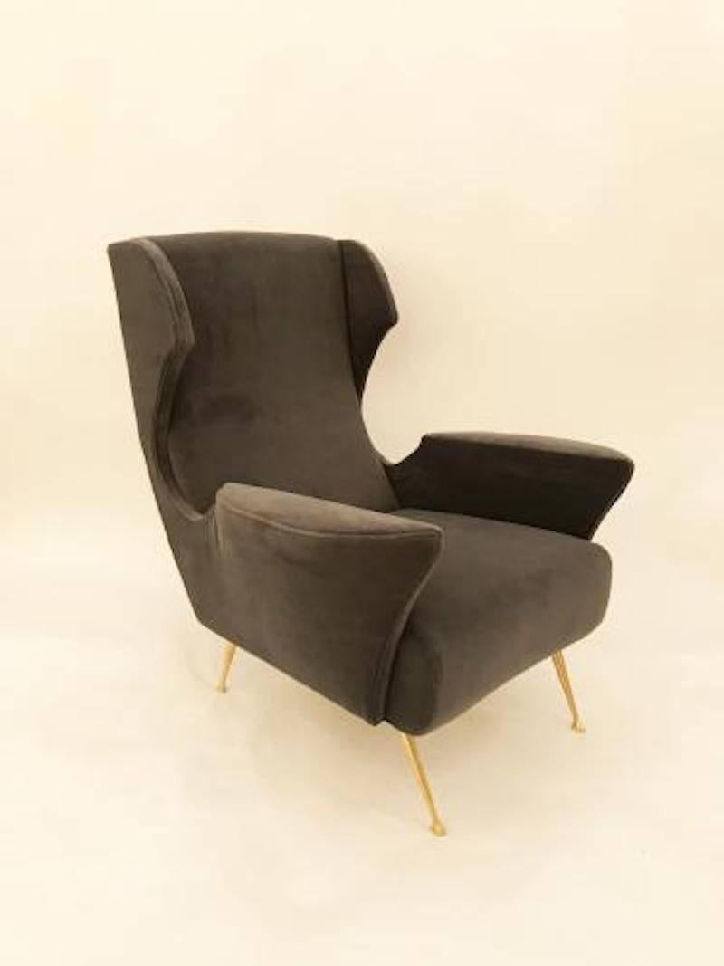 Pair of Mid-Century club chairs each featuring tight seats and back with stylized pointed wings, applied shaped armrests and splayed, tapering brass legs. The clubs have been fully restored and reupholstered in a deep grey velvet. In the style of