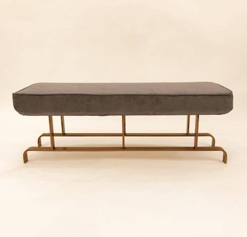 Mid-Century Modernist bench featuring a frame in brass with double stretcher feet. The bench also features all new upholstery done in a grey velvet. The brass has a wonderful age patina. Attributed to Maison Jansen, France, circa 1965.