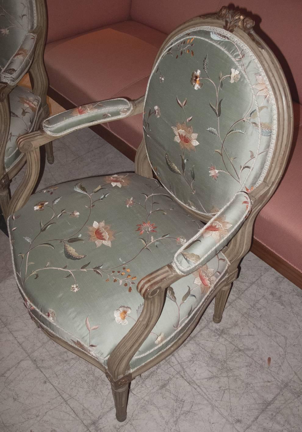 Pair of Louis XVI style grey painted and parcel-gilt fauteuils a La Reine. The chairs upholstered in a high quality silk taffeta with floral embroidery fabric. The fabric in very good condition. The chairs date to the second half of the 19th century.