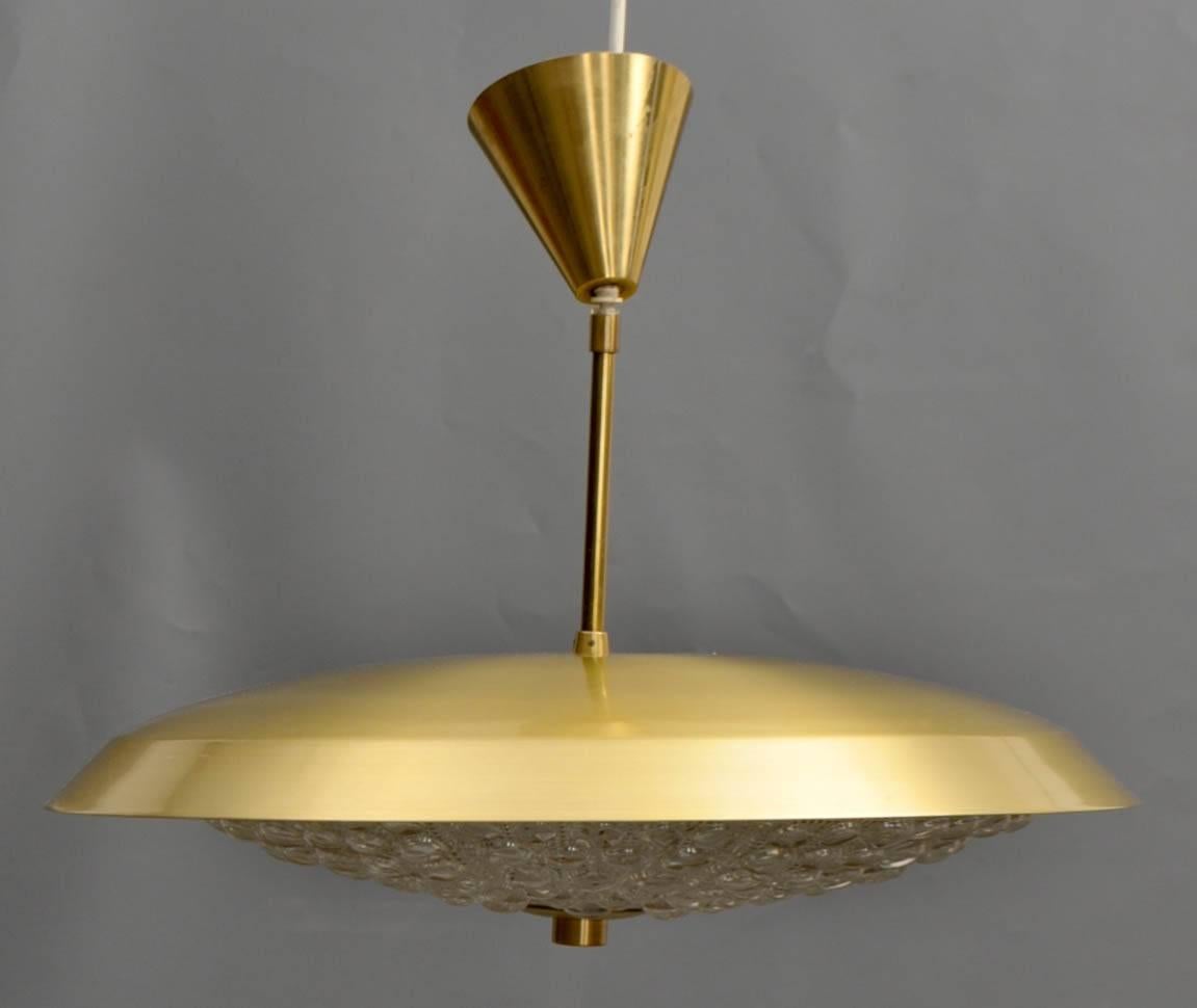 Pendant ceiling fixture of brass and pressed glass designed by Carl Fagerlund for Orrefors of Sweden. The pressed glass bowl mounted with a brass 