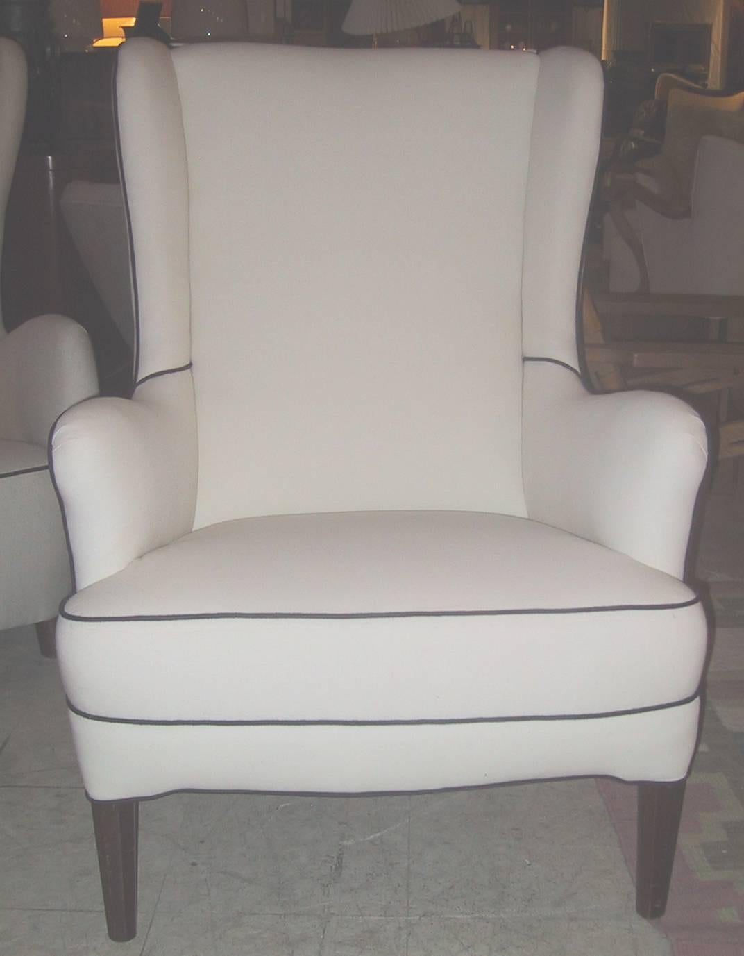 Danish 1940s upholstered large wing chair by Danish designer Frits Henningsen. The chair newly upholstered in a white linen type fabric with black piping. The legs of stained beech.