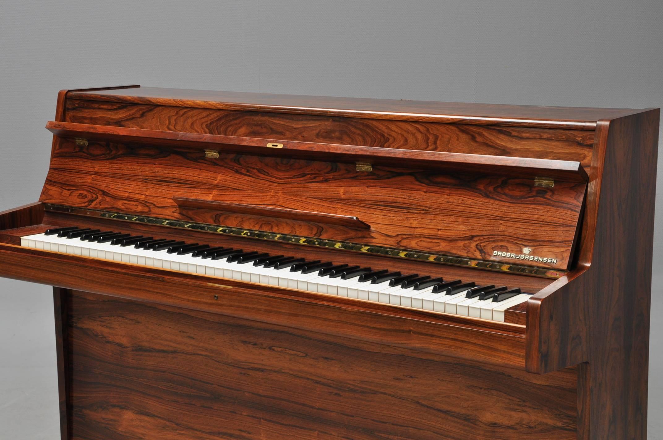 A rare art case Danish console piano of fine quality highly figured rosewood with decorative brass mount above keyboard. By Brodr. Jorgensen, late 1950s-early 1960s. A beautiful piano that works with antiques or modern furniture. This is not your