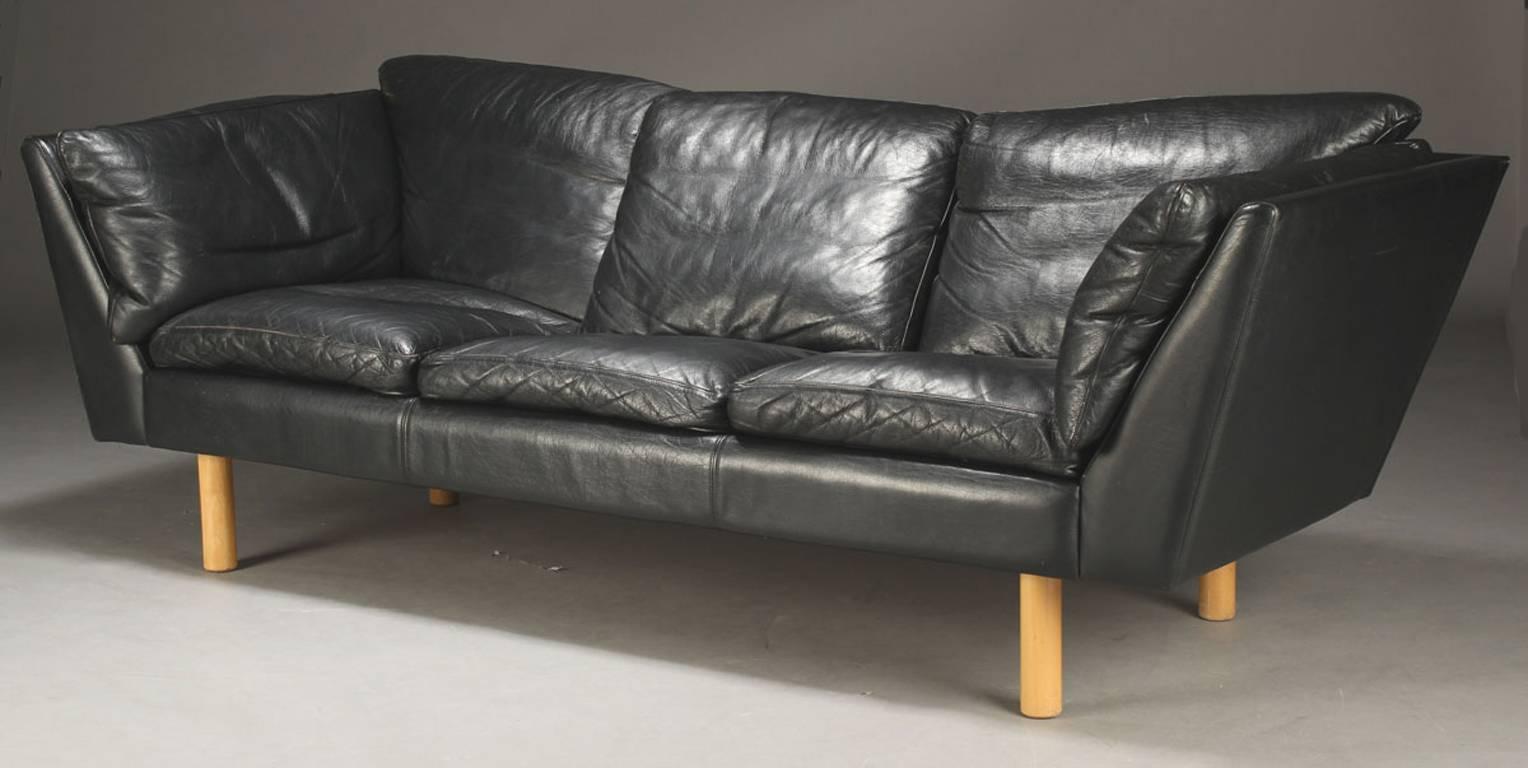 Danish chic black leather upholstered three-seat sofa raised on blonde beech wood legs. By Danish designer Henning Jensen, 1970s-1980s.